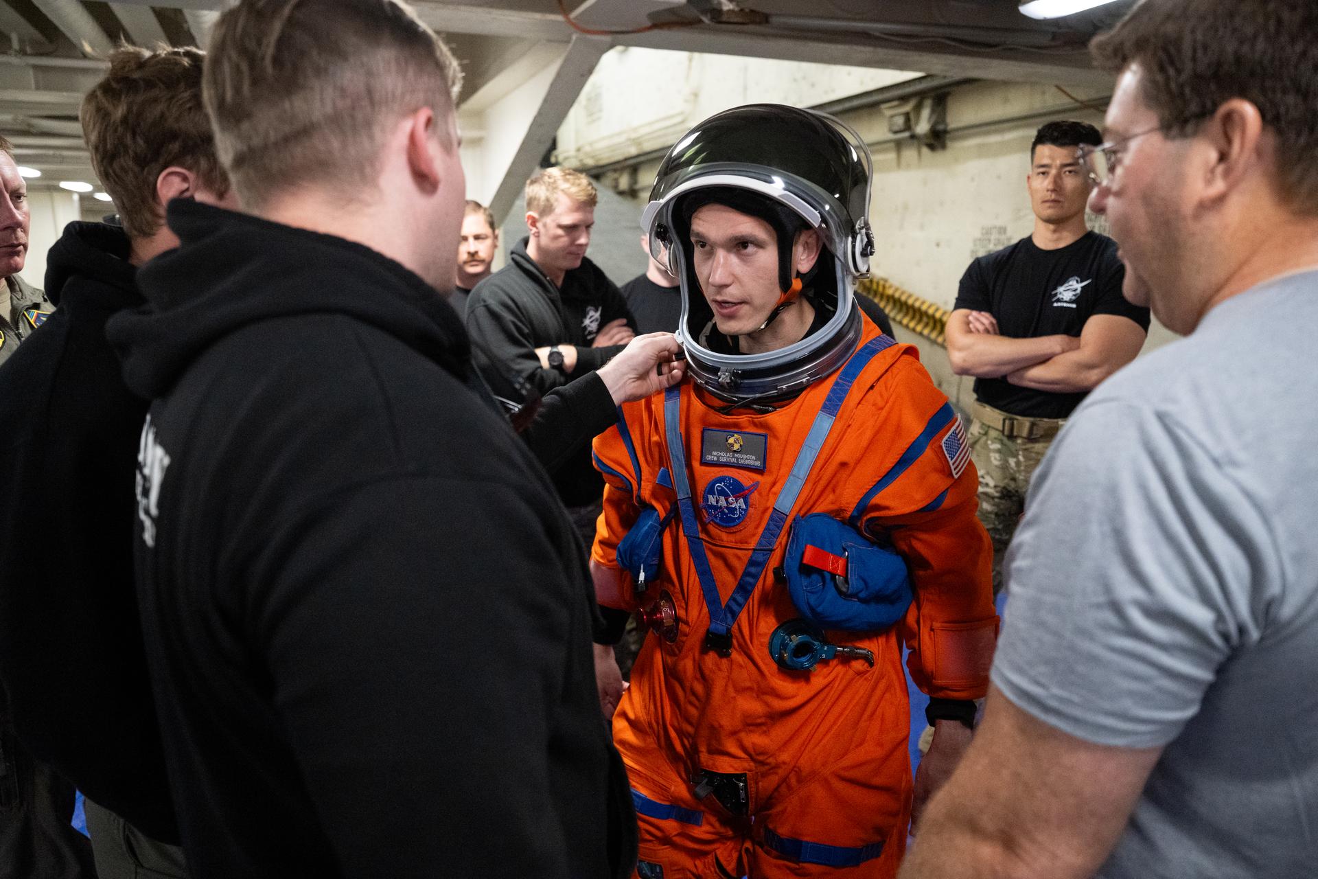 Nicholas Houghton, an Orion Crew Survival System engineer at NASA’s Johnson Space Center, wearing an Orion Crew Survival System suit, conducts familiarization training with U.S. Navy divers on doffing the suit onboard USS John P. Murtha ahead of the return of the Artemis II crewmembers to Earth, Tuesday, April 7, 2026, in the Pacific Ocean off the coast of California. NASA’s Artemis II mission is taking NASA astronauts Reid Wiseman, commander; Victor Glover, pilot; Christina Koch, mission specialist; and CSA (Canadian Space Agency) astronaut Jeremy Hansen, mission specialist on a 10-day journey around the Moon and back aboard their Orion spacecraft. Wiseman, Glover, Koch, and Hansen are scheduled to splash down off the coast of San Diego at approximately 5:07 p.m. PDT (8:07 p.m. EDT) on Friday, April 10.  Photo Credit: (NASA/Joel Kowsky)