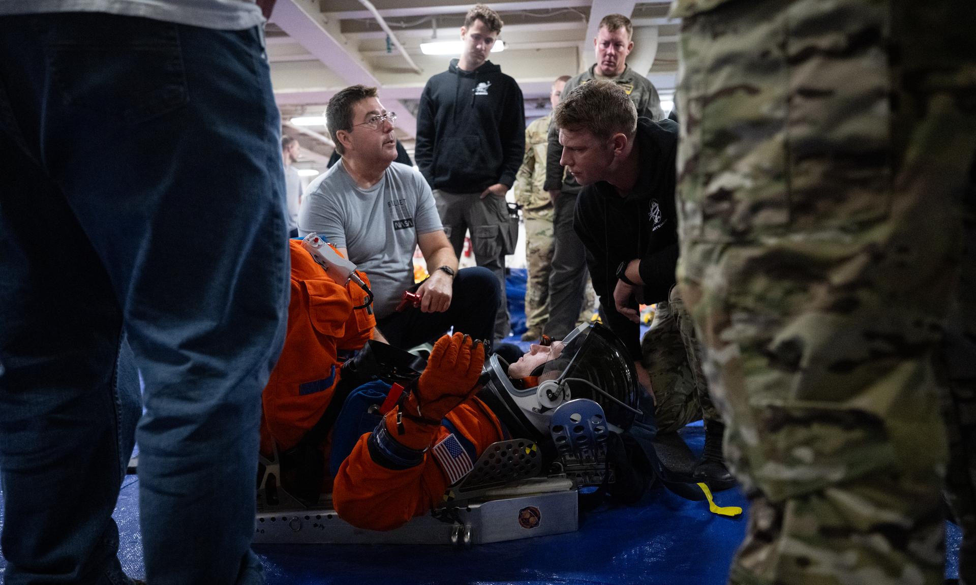 Mike Thompson, an Orion suit technician, left, and Nicholas Houghton, an Orion Crew Survival System engineer at NASA’s Johnson Space Center, wearing an Orion Crew Survival System suit, conducts familiarization training with U.S. Navy divers on doffing the suit onboard USS John P. Murtha ahead of the return of the Artemis II crewmembers to Earth, Tuesday, April 7, 2026, in the Pacific Ocean off the coast of California. NASA’s Artemis II mission is taking NASA astronauts Reid Wiseman, commander; Victor Glover, pilot; Christina Koch, mission specialist; and CSA (Canadian Space Agency) astronaut Jeremy Hansen, mission specialist on a 10-day journey around the Moon and back aboard their Orion spacecraft. Wiseman, Glover, Koch, and Hansen are scheduled to splash down off the coast of San Diego at approximately 5:07 p.m. PDT (8:07 p.m. EDT) on Friday, April 10.  Photo Credit: (NASA/Joel Kowsky)