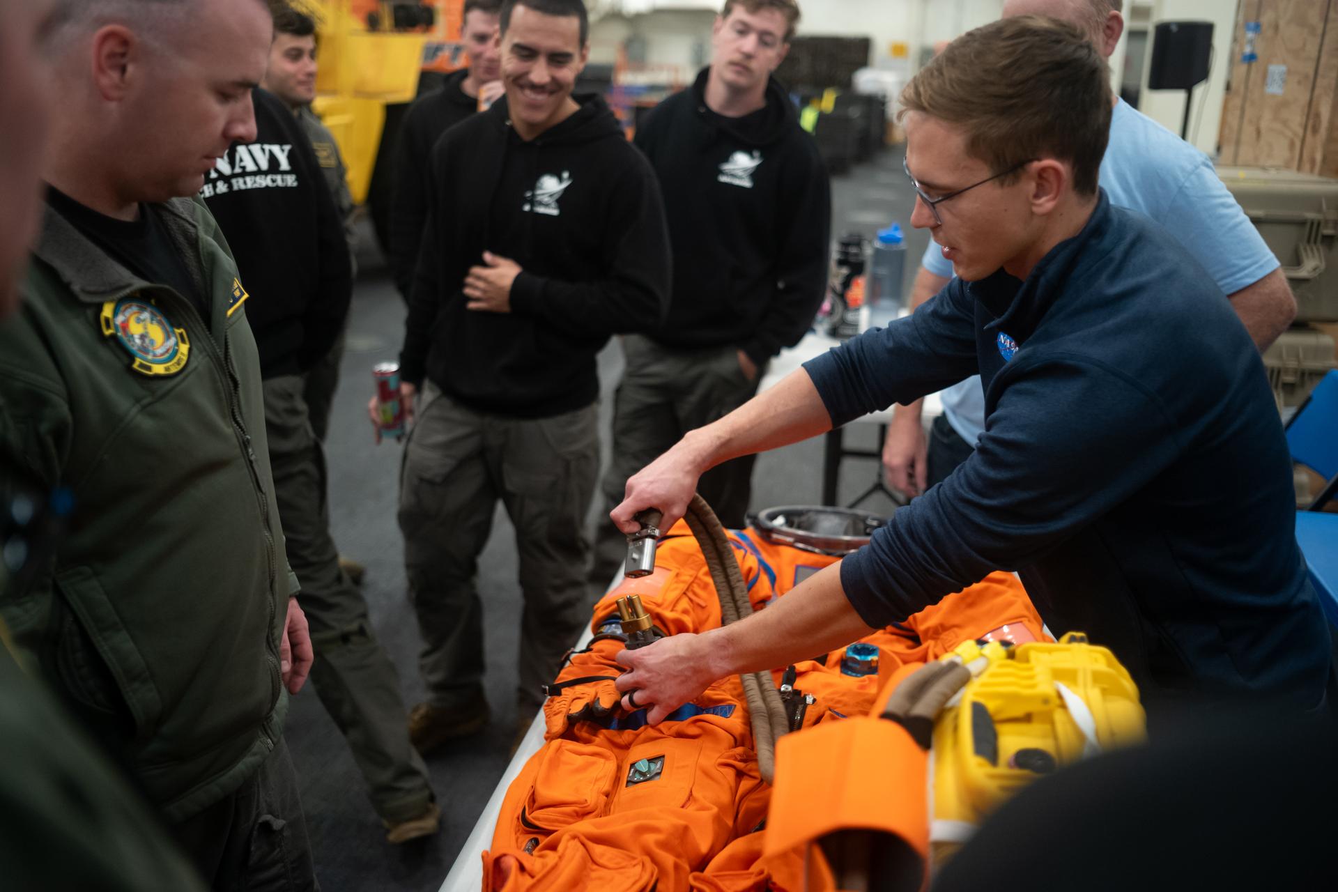 Nicholas Houghton, an Orion Crew Survival System engineer at NASA’s Johnson Space Center, left, conducts familiarization training with the Orion Crew Survival System suit onboard USS John P. Murtha ahead of the return of the Artemis II crewmembers to Earth, Thursday, April 9, 2026, in the Pacific Ocean off the coast of California. NASA’s Artemis II mission is taking NASA astronauts Reid Wiseman, commander; Victor Glover, pilot; Christina Koch, mission specialist; and CSA (Canadian Space Agency) astronaut Jeremy Hansen, mission specialist on a 10-day journey around the Moon and back aboard their Orion spacecraft. Wiseman, Glover, Koch, and Hansen are scheduled to splash down off the coast of San Diego at approximately 5:07 p.m. PDT (8:07 p.m. EDT) on Friday, April 10.  Photo Credit: (NASA/Joel Kowsky)