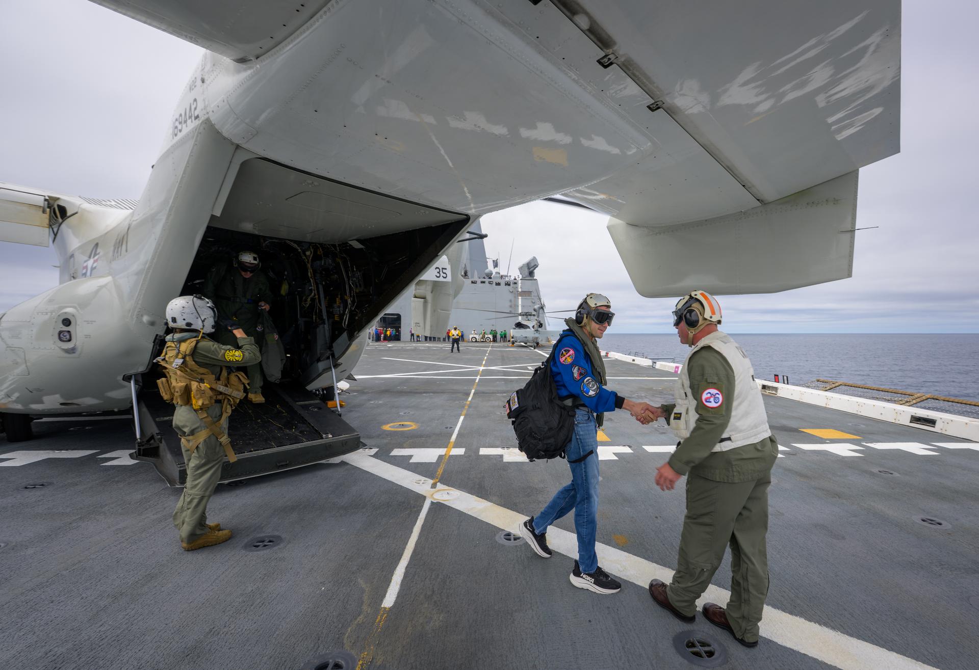 NASA Administrator Jared Isaacman, left, is greeted by Capt. Erik Kenny, commanding officer, USS John P. Murtha (LPD, after a U.S. Navy CMV-22 Osprey landed on the flight deck of USS John P. Murtha with U.S. Navy Rear Adm. Brent DeVore, Commander, Expeditionary Strike Group Three, Michael Altenhofen, senior advisor to the NASA Administrator, and U.S. Air Force Maj. Gen. Michael A. Valle, Deputy Commander, First Air Force, as NASA and U.S. military teams prepare for the the return of the Artemis II crew members to Earth, Friday, April 10, 2026, in the Pacific Ocean off the coast of California. NASA’s Artemis II mission is taking NASA astronauts Reid Wiseman, commander; Victor Glover, pilot; Christina Koch, mission specialist; and CSA (Canadian Space Agency) astronaut Jeremy Hansen, mission specialist on a 10-day journey around the Moon and back aboard their Orion spacecraft. Wiseman, Glover, Koch, and Hansen are scheduled to splash down off the coast of San Diego at approximately 5:07 p.m. PDT (8:07 p.m. EDT). Photo Credit: (NASA/Bill Ingalls)