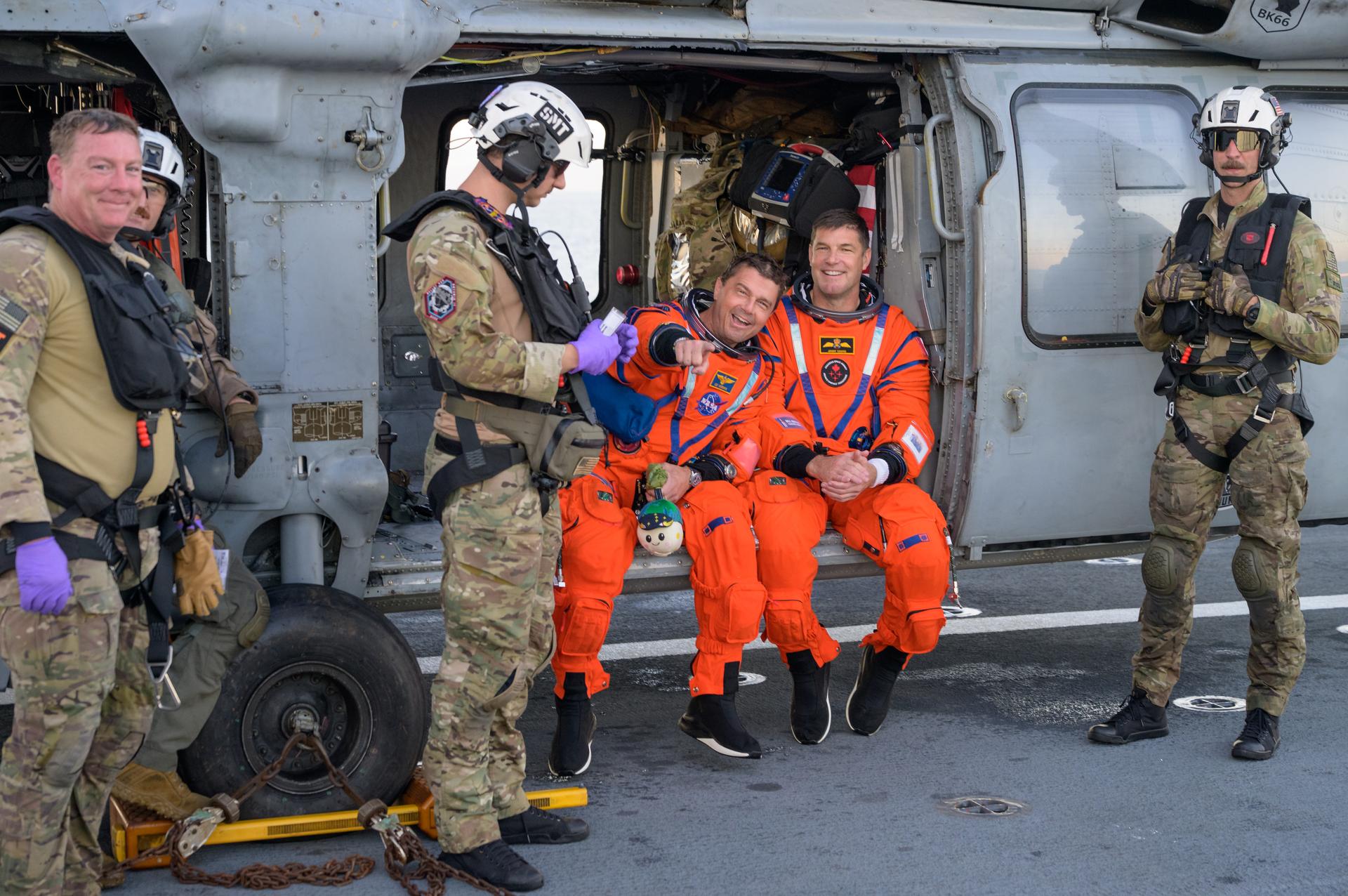 NASA astronaut Reid Wiseman, Artemis II commander, left, and CSA (Canadian Space Agency) astronaut Jeremy Hansen, Artemis II mission specialist, are seen sitting on a Navy MH-60 Seahawk from Helicopter Sea Combat Squadron (HSC) 23 on the flight deck of USS John P. Murtha after they and fellow crewmates NASA astronaut Christina Koch, Artemis II mission specialist, and NASA astronaut Victor Glover, Artemis II pilot, were extracted from their Orion spacecraft after splashdown, Friday, April 10, 2026, in the Pacific Ocean off the coast of California. NASA’s Artemis II mission took the quartet on a nearly 10-day journey around the Moon and back to Earth. Following a splashdown at 5:07 p.m. PDT (8:07 p.m. EDT), NASA, U.S. Navy, and U.S. Air Force teams are working to bring the Orion spacecraft aboard the recovery ship. Photo Credit: (NASA/Bill Ingalls)