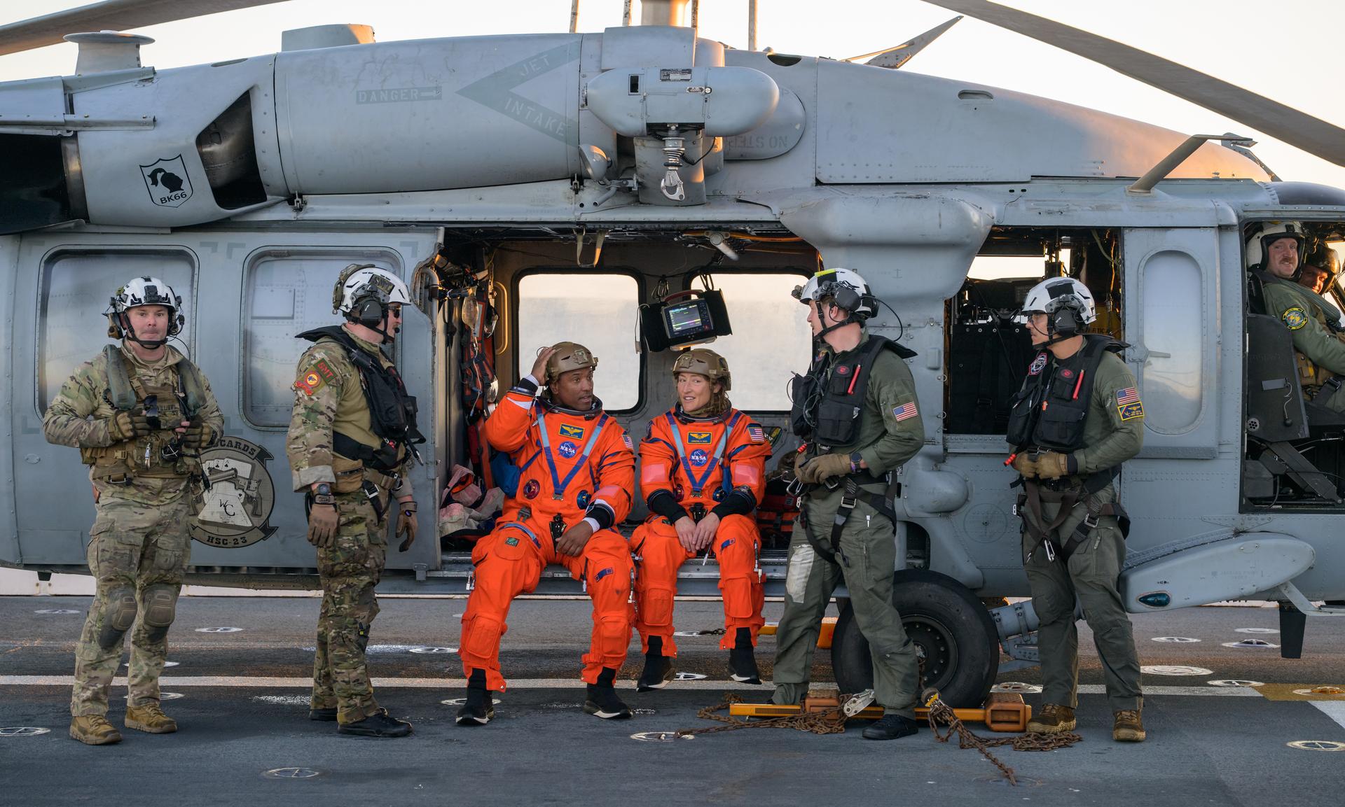 NASA astronaut Victor Glover, Artemis II pilot, left, and NASA astronaut Christina Koch, Artemis II mission specialist are seen sitting on a Navy MH-60 Seahawk from Helicopter Sea Combat Squadron (HSC) 23 on the flight deck of USS John P. Murtha after they and fellow crewmates CSA (Canadian Space Agency) astronaut Jeremy Hansen, Artemis II mission specialist, and NASA astronaut Reid Wiseman, Artemis II commander, were extracted from their Orion spacecraft after splashdown, Friday, April 10, 2026, in the Pacific Ocean off the coast of California. NASA’s Artemis II mission took the quartet on a nearly 10-day journey around the Moon and back to Earth. Following a splashdown at 5:07 p.m. PDT (8:07 p.m. EDT), NASA, U.S. Navy, and U.S. Air Force teams are working to bring the Orion spacecraft aboard the recovery ship. Photo Credit: (NASA/Bill Ingalls)
