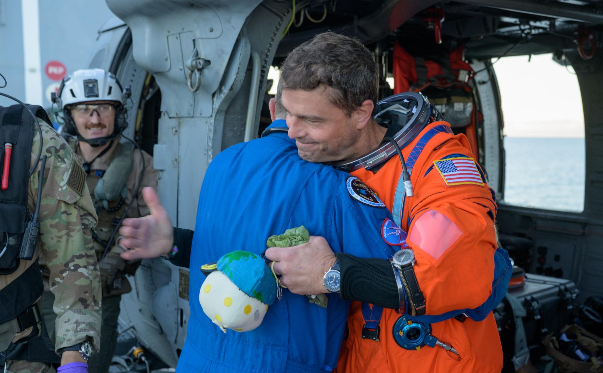 NASA astronaut Reid Wiseman, Artemis II commander, gives NASA Flight Surgeon Richard Scheuring a hug next to a Navy MH-60 Seahawk from Helicopter Sea Combat Squadron (HSC) 23 on the flight deck of USS John P. Murtha after he and fellow crewmates NASA Astronauts Victor Glover,  Christina Koch, and CSA (Canadian Space Agency) astronaut Jeremy Hansen, were extracted from their Orion spacecraft after splashdown, Friday, April 10, 2026, in the Pacific Ocean off the coast of California. NASA’s Artemis II mission took the quartet on a nearly 10-day journey around the Moon and back to Earth. Following a splashdown at 5:07 p.m. PDT (8:07 p.m. EDT), NASA, U.S. Navy, and U.S. Air Force teams are working to bring the Orion spacecraft aboard the recovery ship. Photo Credit: (NASA/Bill Ingalls)