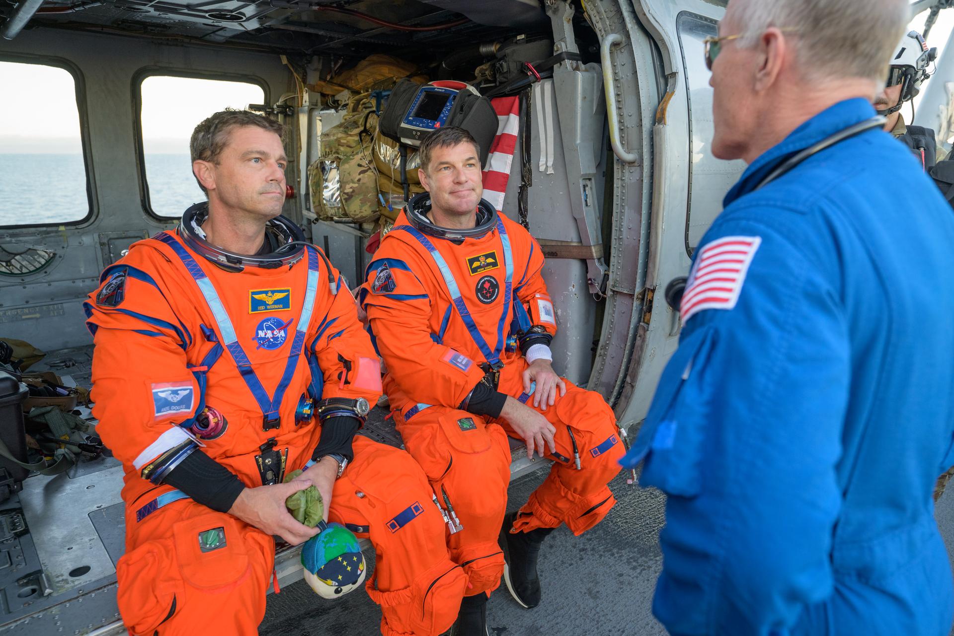 NASA astronaut Reid Wiseman, Artemis II commander, left, and CSA (Canadian Space Agency) astronaut Jeremy Hansen, Artemis II mission specialist, talk with NASA Flight Surgeon Richard Scheuring at their Navy MH-60 Seahawk from Helicopter Sea Combat Squadron (HSC) 23 on the flight deck of USS John P. Murtha after they and fellow crewmates NASA Astronauts Victor Glover, and Christina Koch were extracted from their Orion spacecraft after splashdown, Friday, April 10, 2026, in the Pacific Ocean off the coast of California. NASA’s Artemis II mission took the quartet on a nearly 10-day journey around the Moon and back to Earth. Following a splashdown at 5:07 p.m. PDT (8:07 p.m. EDT), NASA, U.S. Navy, and U.S. Air Force teams are working to bring the Orion spacecraft aboard the recovery ship. Photo Credit: (NASA/Bill Ingalls)