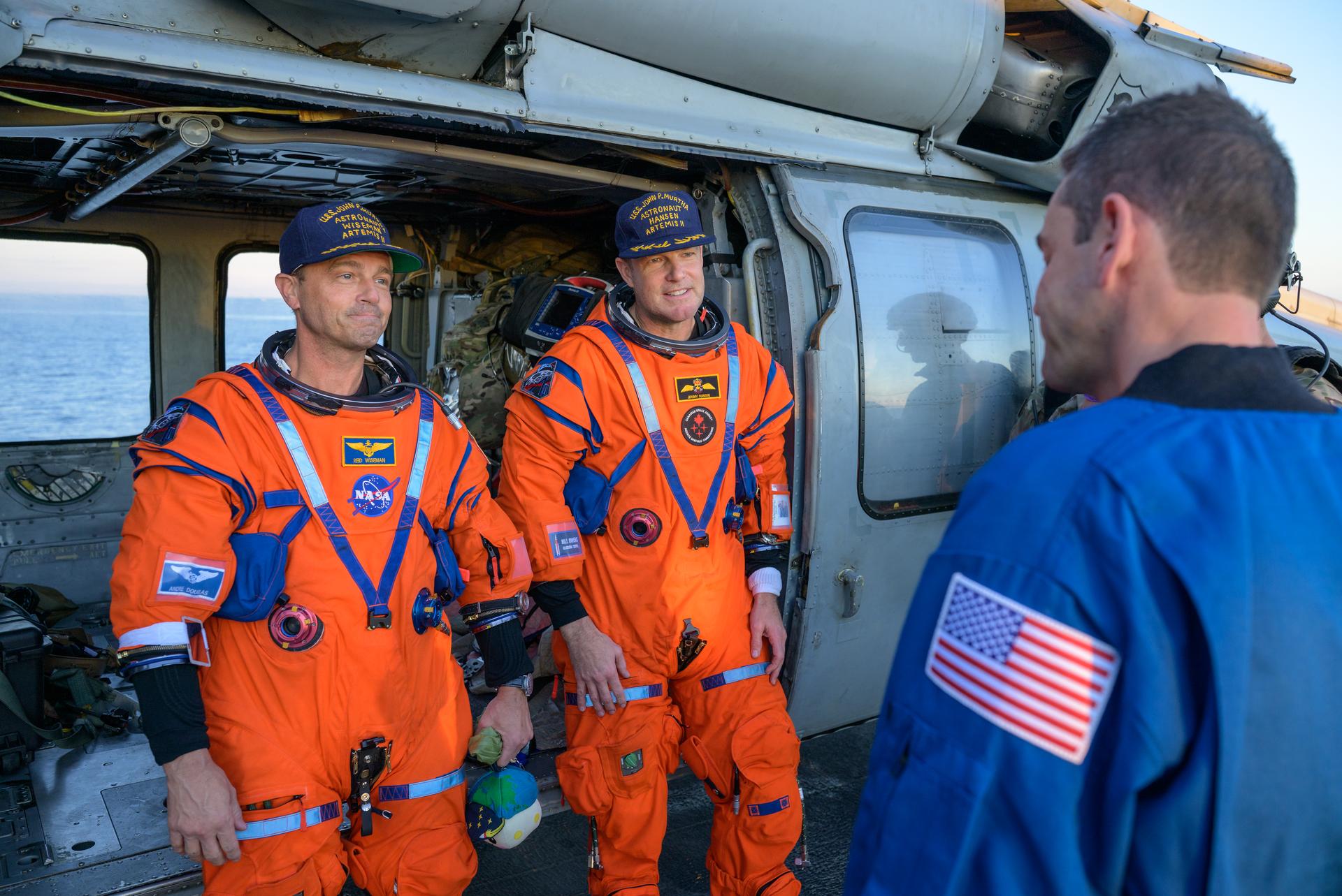 NASA astronaut Reid Wiseman, Artemis II commander, left, and CSA (Canadian Space Agency) astronaut Jeremy Hansen, Artemis II mission specialist, talk with NASA Flight Surgeon Richard Scheuring at their Navy MH-60 Seahawk from Helicopter Sea Combat Squadron (HSC) 23 on the flight deck of USS John P. Murtha after they and fellow crewmates NASA Astronauts Victor Glover, and Christina Koch were extracted from their Orion spacecraft after splashdown, Friday, April 10, 2026, in the Pacific Ocean off the coast of California. NASA’s Artemis II mission took the quartet on a nearly 10-day journey around the Moon and back to Earth. Following a splashdown at 5:07 p.m. PDT (8:07 p.m. EDT), NASA, U.S. Navy, and U.S. Air Force teams are working to bring the Orion spacecraft aboard the recovery ship. Photo Credit: (NASA/Bill Ingalls)