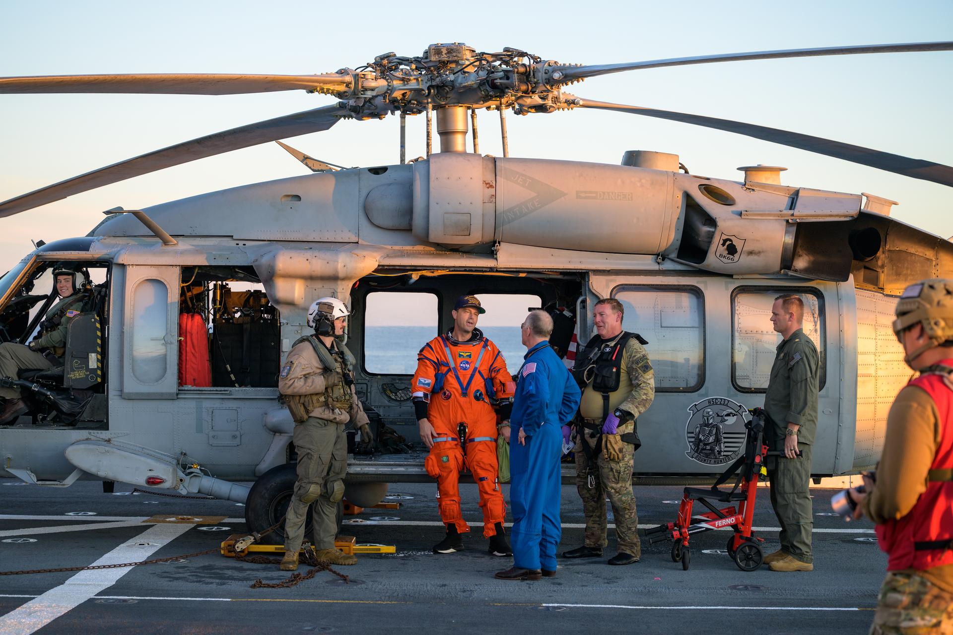 NASA astronaut Reid Wiseman, Artemis II commander is seen standing next to a Navy MH-60 Seahawk from Helicopter Sea Combat Squadron (HSC) 23 talking with NASA Flight Surgeon Richard Scheuring on the flight deck of USS John P. Murtha after he and fellow crewmates NASA Astronauts Victor Glover, Christina Koch, and CSA (Canadian Space Agency) astronaut Jeremy Hansen, were extracted from their Orion spacecraft after splashdown, Friday, April 10, 2026, in the Pacific Ocean off the coast of California. NASA’s Artemis II mission took the quartet on a nearly 10-day journey around the Moon and back to Earth. Following a splashdown at 5:07 p.m. PDT (8:07 p.m. EDT), NASA, U.S. Navy, and U.S. Air Force teams are working to bring the Orion spacecraft aboard the recovery ship. Photo Credit: (NASA/Bill Ingalls)