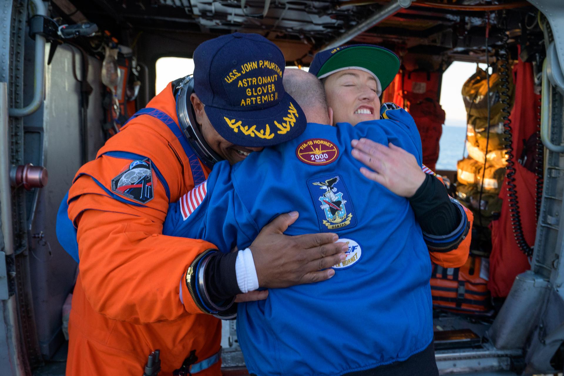 NASA astronaut Victor Glover, Artemis II pilot, left, and NASA astronaut Christina Koch, Artemis II mission specialist, right, hug Scott Tingle, Chief of the Astronaut Office next to a Navy MH-60 Seahawk from Helicopter Sea Combat Squadron (HSC) 23 on the flight deck of USS John P. Murtha after they and fellow crewmates CSA (Canadian Space Agency) astronaut Jeremy Hansen, Artemis II mission specialist, and NASA astronaut Reid Wiseman, Artemis II commander, were extracted from their Orion spacecraft after splashdown, Friday, April 10, 2026, in the Pacific Ocean off the coast of California. NASA’s Artemis II mission took the quartet on a nearly 10-day journey around the Moon and back to Earth. Following a splashdown at 5:07 p.m. PDT (8:07 p.m. EDT), NASA, U.S. Navy, and U.S. Air Force teams are working to bring the Orion spacecraft aboard the recovery ship. Photo Credit: (NASA/Bill Ingalls)