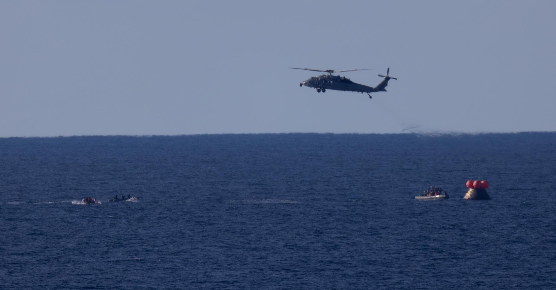 A U.S. Navy MH-60 Seahawks from Helicopter Sea Combat Squadron (HSC) 23 flies overhead as small boats approach NASA’s Orion spacecraft with Artemis II crewmembers NASA astronauts Reid Wiseman, commander; Victor Glover, pilot; Christina Koch, mission specialist; and CSA (Canadian Space Agency) astronaut Jeremy Hansen, mission specialist aboard is seen after landing as recovery teams as NASA’s Landing and Recovery team, along with U.S. Navy personnel in small boats begin to approach the spacecraft in the Pacific Ocean off the coast of California, Friday, April 10, 2026. NASA’s Artemis II mission took Wiseman, Glover, Koch, and Hansen on a nearly 10-day journey around the Moon and back to Earth. Following a splashdown at 5:07 p.m. PDT (8:07 p.m. EDT), NASA and U.S. military teams are working to bring the crewmembers and Orion spacecraft aboard USS John P. Murtha.  Photo Credit: (NASA/Joel Kowsky)