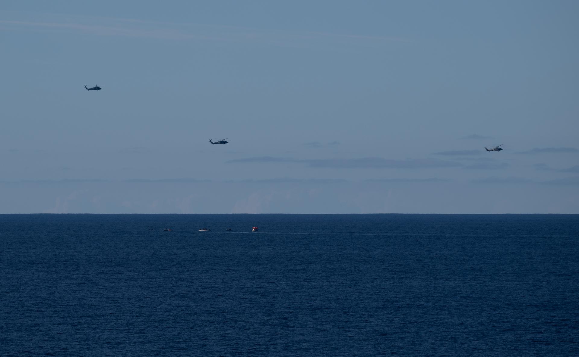 Three U.S. Navy MH-60 Seahawks from Helicopter Sea Combat Squadron (HSC) 23 flies overhead as small boats approach NASA’s Orion spacecraft with Artemis II crewmembers NASA astronauts Reid Wiseman, commander; Victor Glover, pilot; Christina Koch, mission specialist; and CSA (Canadian Space Agency) astronaut Jeremy Hansen, mission specialist aboard is seen after landing as recovery teams as NASA’s Landing and Recovery team, along with U.S. Navy personnel in small boats begin to approach the spacecraft in the Pacific Ocean off the coast of California, Friday, April 10, 2026. NASA’s Artemis II mission took Wiseman, Glover, Koch, and Hansen on a nearly 10-day journey around the Moon and back to Earth. Following a splashdown at 5:07 p.m. PDT (8:07 p.m. EDT), NASA and U.S. military teams are working to bring the crewmembers and Orion spacecraft aboard USS John P. Murtha.  Photo Credit: (NASA/Joel Kowsky)