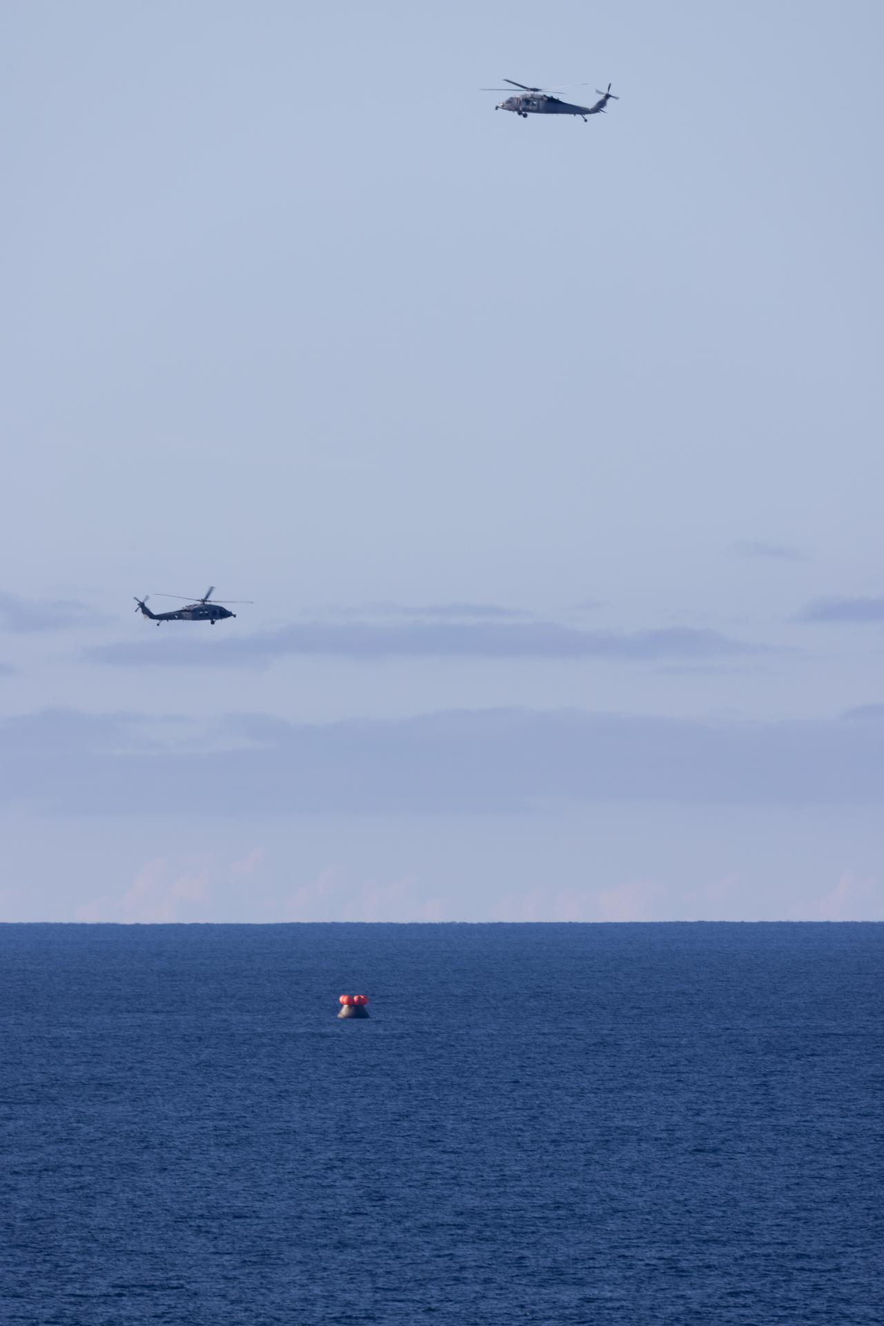Two U.S. Navy MH-60 Seahawks from Helicopter Sea Combat Squadron (HSC) 23 flies overhead as small boats approach NASA’s Orion spacecraft with Artemis II crewmembers NASA astronauts Reid Wiseman, commander; Victor Glover, pilot; Christina Koch, mission specialist; and CSA (Canadian Space Agency) astronaut Jeremy Hansen, mission specialist aboard is seen after landing as recovery teams as NASA’s Landing and Recovery team, along with U.S. Navy personnel in small boats begin to approach the spacecraft in the Pacific Ocean off the coast of California, Friday, April 10, 2026. NASA’s Artemis II mission took Wiseman, Glover, Koch, and Hansen on a nearly 10-day journey around the Moon and back to Earth. Following a splashdown at 5:07 p.m. PDT (8:07 p.m. EDT), NASA and U.S. military teams are working to bring the crewmembers and Orion spacecraft aboard USS John P. Murtha.  Photo Credit: (NASA/Joel Kowsky)