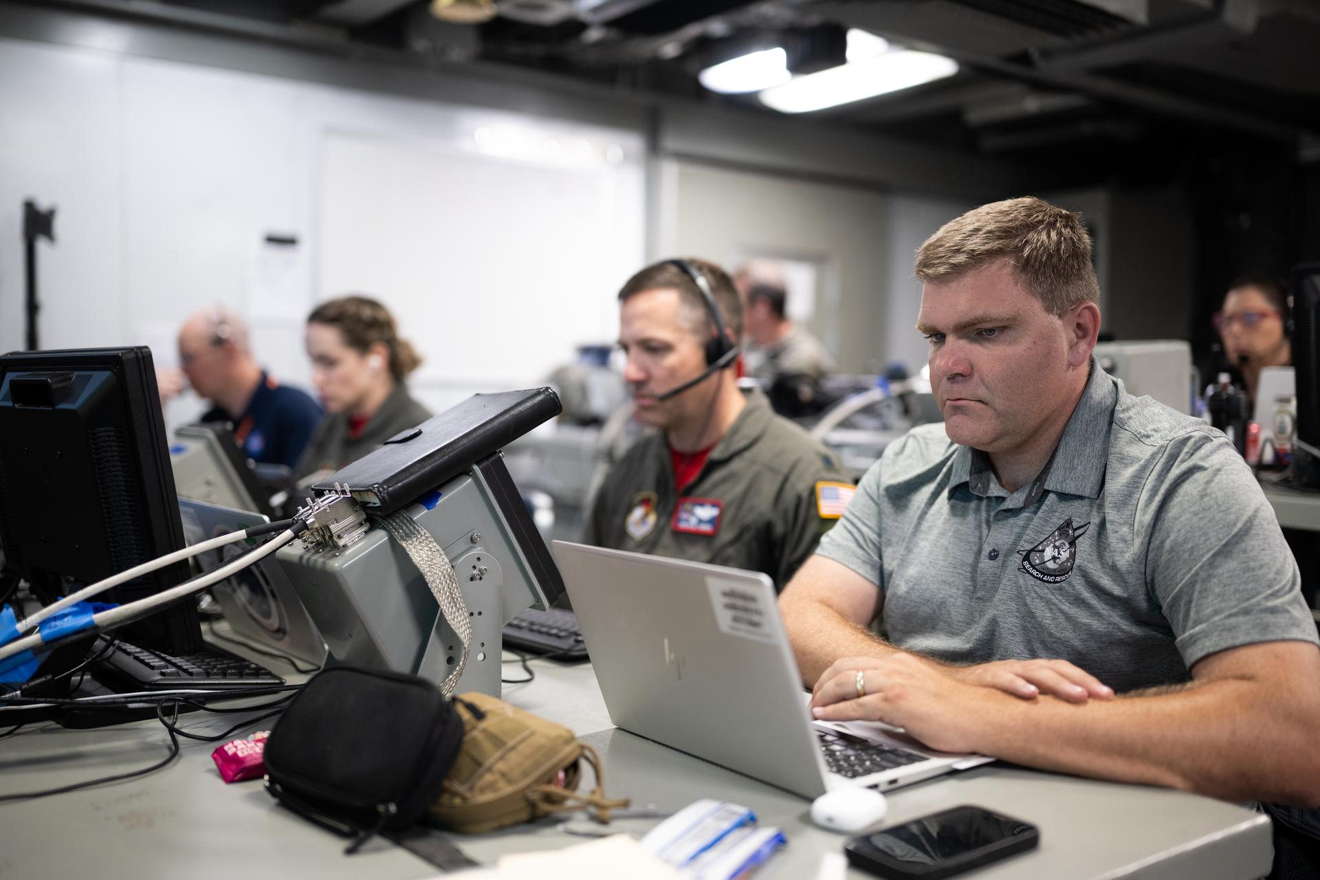 Cody Kelly, deputy for national affairs in the Search and Rescue Office at NASA’s Goddard Space Flight Center is seen alongside NASA and U.S. military recovery team members as they work inside the Landing Force Operations Center onboard USS John P. Murtha monitoring the recovery of NASA’s Orion spacecraft with Artemis II crewmembers NASA astronauts Reid Wiseman, commander; Victor Glover, pilot; Christina Koch, mission specialist; and CSA (Canadian Space Agency) astronaut Jeremy Hansen, mission specialist aboard in the Pacific Ocean off the coast of California, Friday, April 10, 2026. NASA’s Artemis II mission took Wiseman, Glover, Koch, and Hansen on a 10-day journey around the Moon and back to Earth. Following a splashdown at 5:07 p.m. PDT (8:07 p.m. EDT), NASA and U.S. military teams worked to bring the crewmembers and Orion spacecraft aboard USS John P. Murtha.  Photo Credit: (NASA/Joel Kowsky)