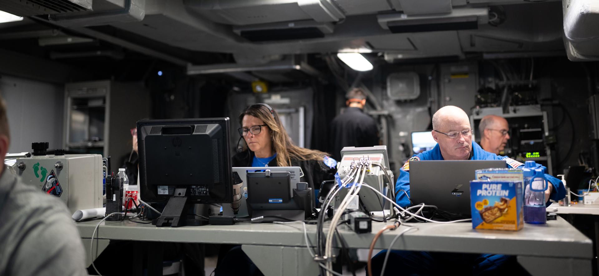 Lisa Seiler, Artemis II landing and recovery deputy director, left, and Scott Tingle, Chief of the Astronaut Office, right, are seen alongside other NASA and U.S. military recovery team members as they work inside the Landing Force Operations Center onboard USS John P. Murtha monitoring the recovery of NASA’s Orion spacecraft with Artemis II crewmembers NASA astronauts Reid Wiseman, commander; Victor Glover, pilot; Christina Koch, mission specialist; and CSA (Canadian Space Agency) astronaut Jeremy Hansen, mission specialist aboard in the Pacific Ocean off the coast of California, Friday, April 10, 2026. NASA’s Artemis II mission took Wiseman, Glover, Koch, and Hansen on a 10-day journey around the Moon and back to Earth. Following a splashdown at 5:07 p.m. PDT (8:07 p.m. EDT), NASA and U.S. military teams worked to bring the crewmembers and Orion spacecraft aboard USS John P. Murtha.  Photo Credit: (NASA/Joel Kowsky)