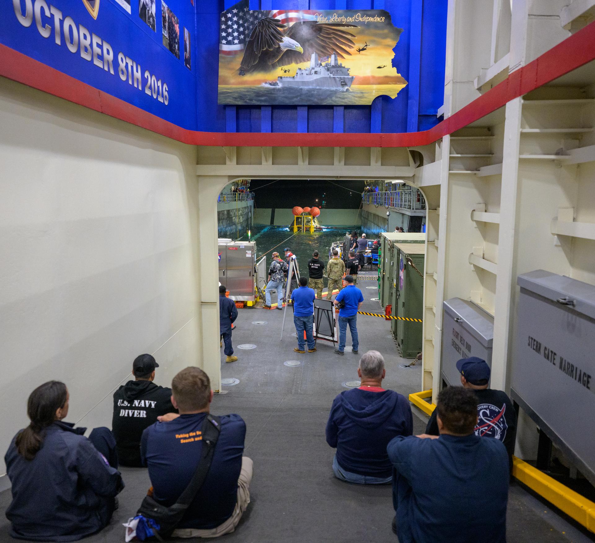 NASA’s Landing and Recovery team, along with U.S. Navy personnel work to recover the spacecraft into the well deck of USS John P. Murtha in the Pacific Ocean off the coast of California, Saturday, April 11, 2026. NASA’s Artemis II mission, which took NASA astronauts Reid Wiseman, commander; Victor Glover, pilot; Christina Koch, mission specialist; and CSA (Canadian Space Agency) astronaut Jeremy Hansen, mission specialist on a 10-day journey around the Moon and back to Earth, splashed down at at 5:07 p.m. PDT (8:07 p.m. EDT).  Photo Credit: (NASA/Bill Ingalls)