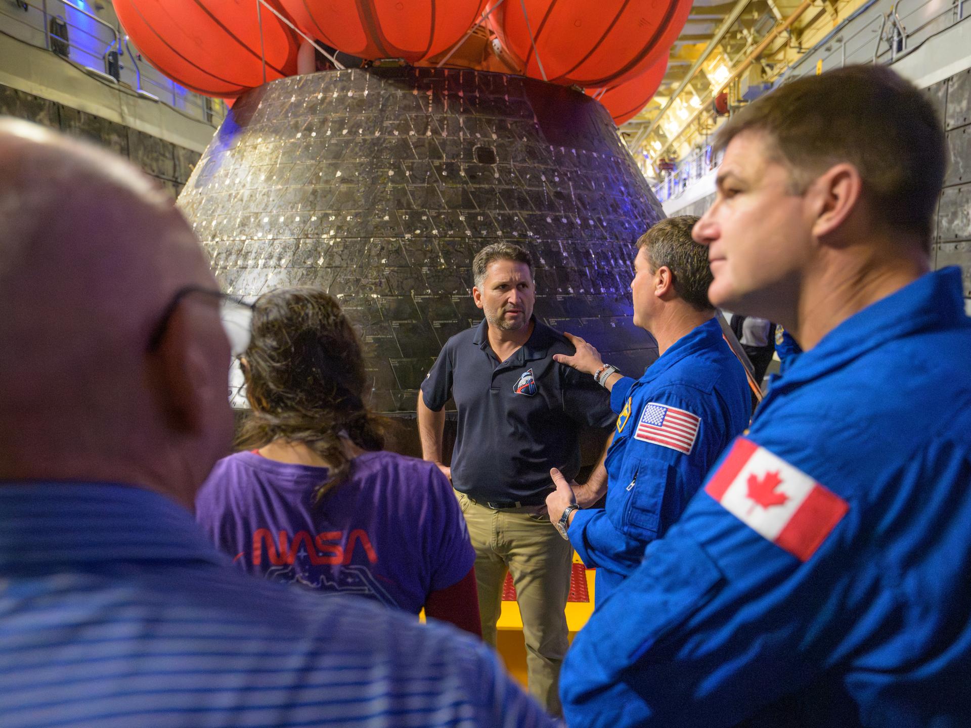 NASA Orion Vehicle Integration Manager Luis Saucedo, center, talks about the Orion spacecraft with NASA astronaut Reid Wiseman, commander; CSA (Canadian Space Agency) astronaut Jeremy Hansen, mission specialist, right, and others in the well deck of USS John P. Murtha, Saturday, April 11, 2026, in the Pacific Ocean off the coast of California. The Artemis II crew splashed down Friday, April 10 at 5:07 p.m. PDT (8:07p.m. EDT). Photo Credit: (NASA/Bill Ingalls)