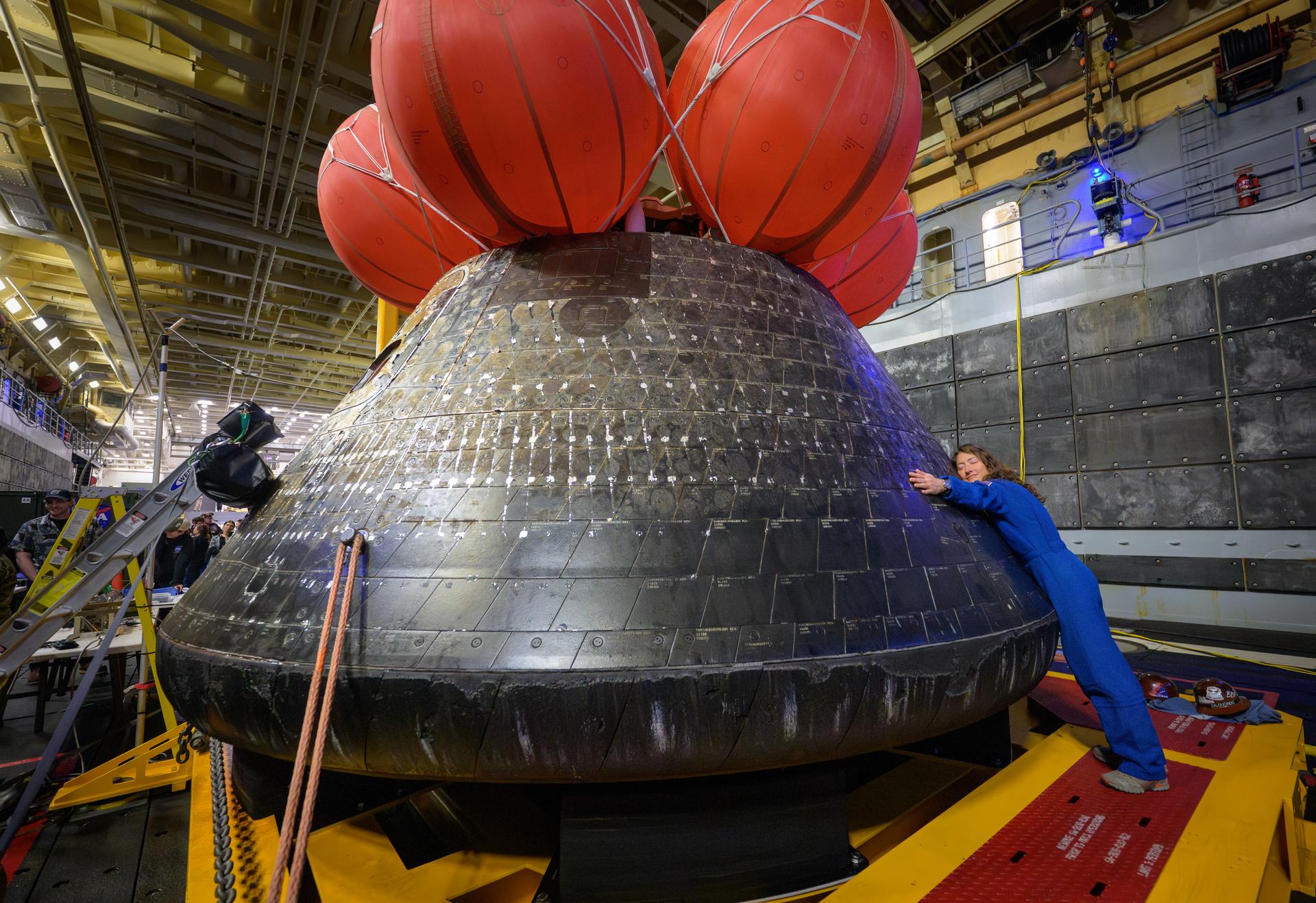 NASA astronaut Christina Koch, Artemis II mission specialist hugs the Orion spacecraft in the well deck of USS John P. Murtha, Saturday, April 11, 2026, in the Pacific Ocean off the coast of California. Koch, NASA astronaut Reid Wiseman, Artemis II commander, NASA astronaut Victor Glover, Artemis II pilot, and CSA (Canadian Space Agency) astronaut Jeremy Hansen, mission specialist; splashed down in the Pacific Ocean, Friday, April 10 at 5:07 p.m. PDT (8:07p.m. EDT). Photo Credit: (NASA/Bill Ingalls)