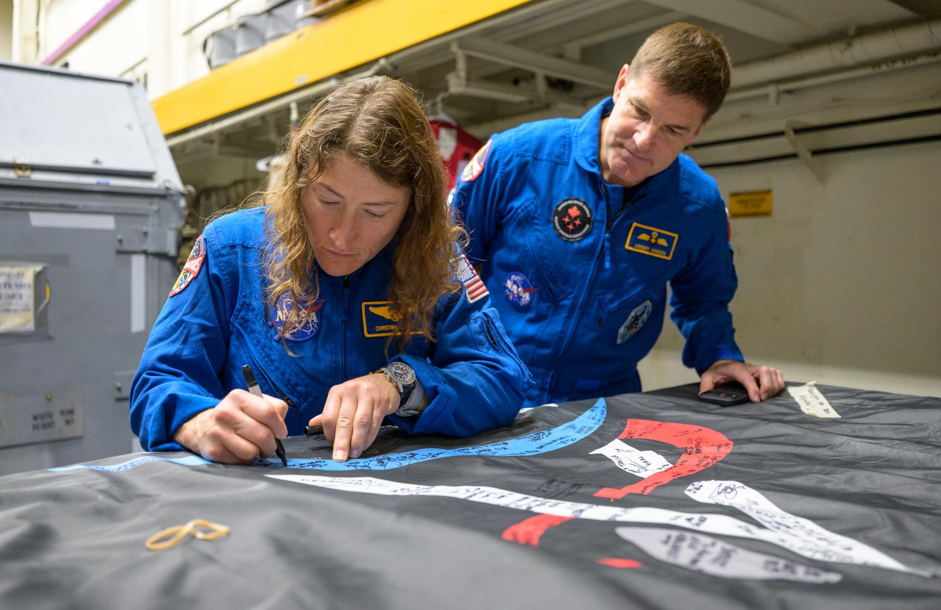 NASA astronaut Christina Koch, Artemis II mission specialist signs an Artemis II flag, as CSA (Canadian Space Agency) astronaut Jeremy Hansen, Artemis II mission specialist looks on, onboard USS John P. Murtha, Saturday, April 11, 2026, in the Pacific Ocean off the coast of California. Koch, Hansen, NASA astronaut Victor Glover, Artemis II pilot, and NASA astronaut Reid Wiseman, Artemis II commander, splashed down in the Pacific Ocean, Friday, April 10 at 5:07 p.m. PDT (8:07p.m. EDT). Photo Credit: (NASA/Bill Ingalls)