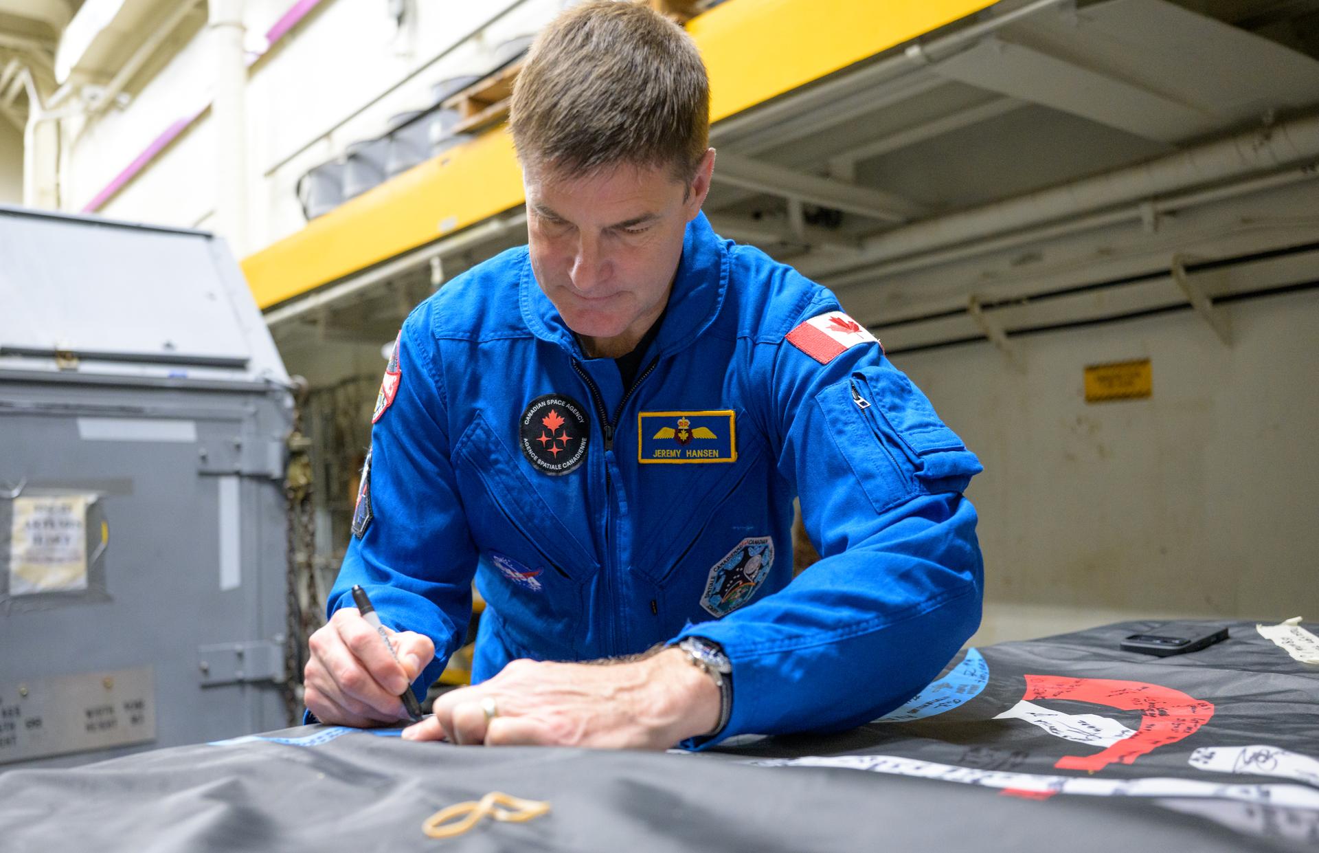 CSA (Canadian Space Agency) astronaut Jeremy Hansen, Artemis II mission specialist signs an Artemis II flag, onboard USS John P. Murtha, Saturday, April 11, 2026, in the Pacific Ocean off the coast of California. Hansen, and NASA astronauts Victor Glover, Artemis II pilot, Reid Wiseman, Artemis II commander, and Christina Koch, Artemis II mission specialist, splashed down in the Pacific Ocean, Friday, April 10 at 5:07 p.m. PDT (8:07p.m. EDT). Photo Credit: (NASA/Bill Ingalls)