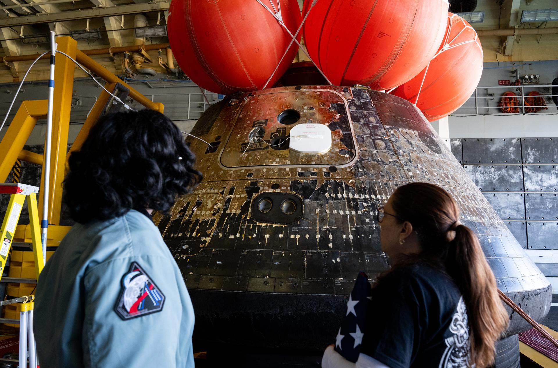 Lilian Villarreal, Artemis II landing and recovery director for Exploration Ground Systems at NASA's Kennedy Space Center, left, and Lakiesha Hawkins, acting deputy associate administrator for NASA's Exploration Systems Development Mission Directorate, right, are seen as they walk around the agency’s Orion spacecraft in the well deck of USS John P. Murtha, Saturday, April 11, 2026, at Naval Base San Diego in California. NASA’s Artemis II mission, which took NASA astronauts Reid Wiseman, commander; Victor Glover, pilot; Christina Koch, mission specialist; and CSA (Canadian Space Agency) astronaut Jeremy Hansen, mission specialist on a nearly 10-day journey around the Moon and back to Earth, splashed down at 5:07 p.m. PDT (8:07 p.m. EDT) on April 10 in the Pacific Ocean off the coast of California.  Photo Credit: (NASA/Joel Kowsky)