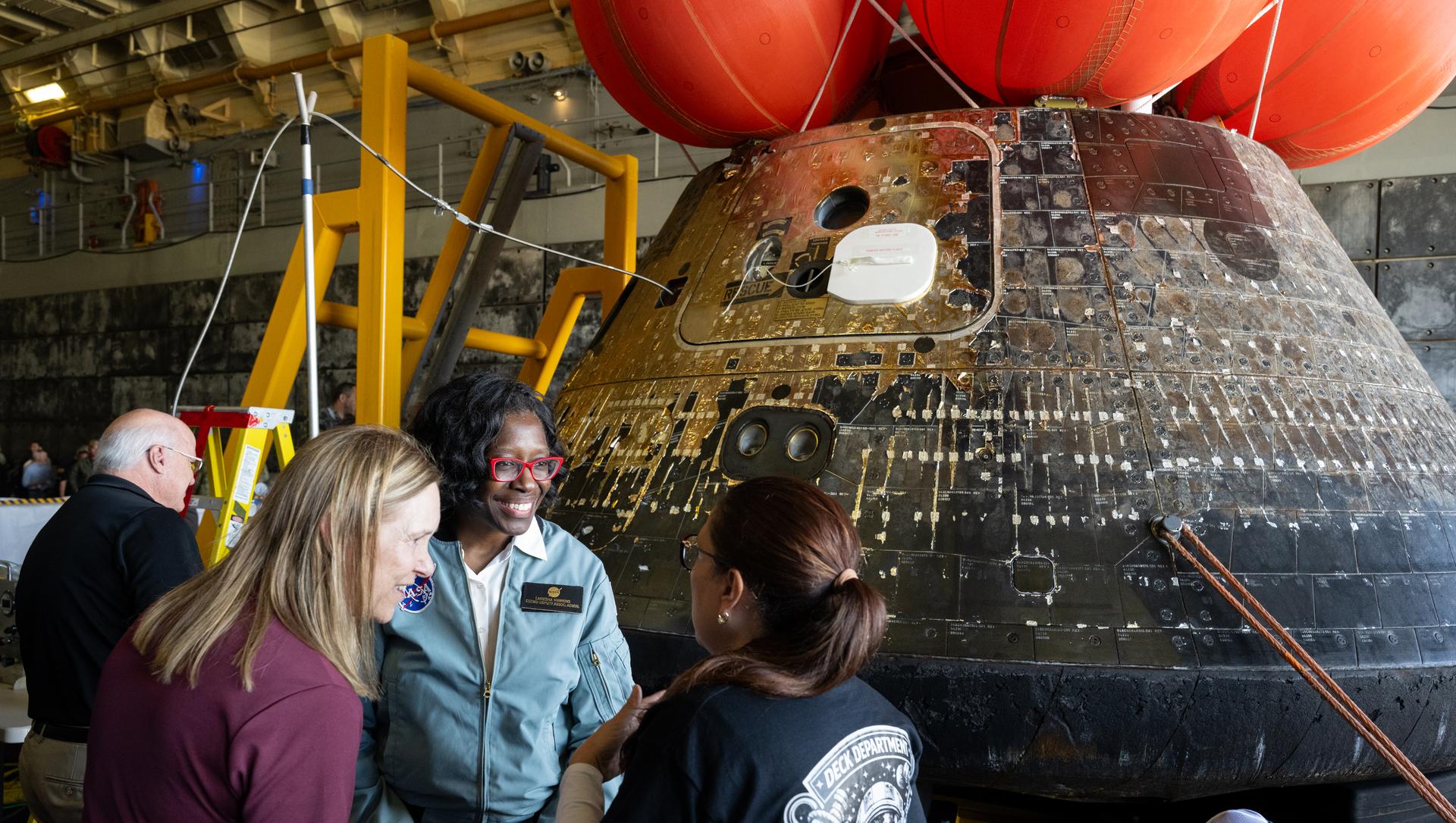 Lilian Villarreal, Artemis II landing and recovery director for Exploration Ground Systems at NASA's Kennedy Space Center, right, speaks with Janet Petro, director of NASA's Kennedy Space Center, left, and Lakiesha Hawkins, acting deputy associate administrator for NASA's Exploration Systems Development Mission Directorate, center, as they look at the agency’s Orion spacecraft in the well deck of USS John P. Murtha, Saturday, April 11, 2026, at Naval Base San Diego in California. NASA’s Artemis II mission, which took NASA astronauts Reid Wiseman, commander; Victor Glover, pilot; Christina Koch, mission specialist; and CSA (Canadian Space Agency) astronaut Jeremy Hansen, mission specialist on a nearly 10-day journey around the Moon and back to Earth, splashed down at 5:07 p.m. PDT (8:07 p.m. EDT) on April 10 in the Pacific Ocean off the coast of California.  Photo Credit: (NASA/Joel Kowsky)