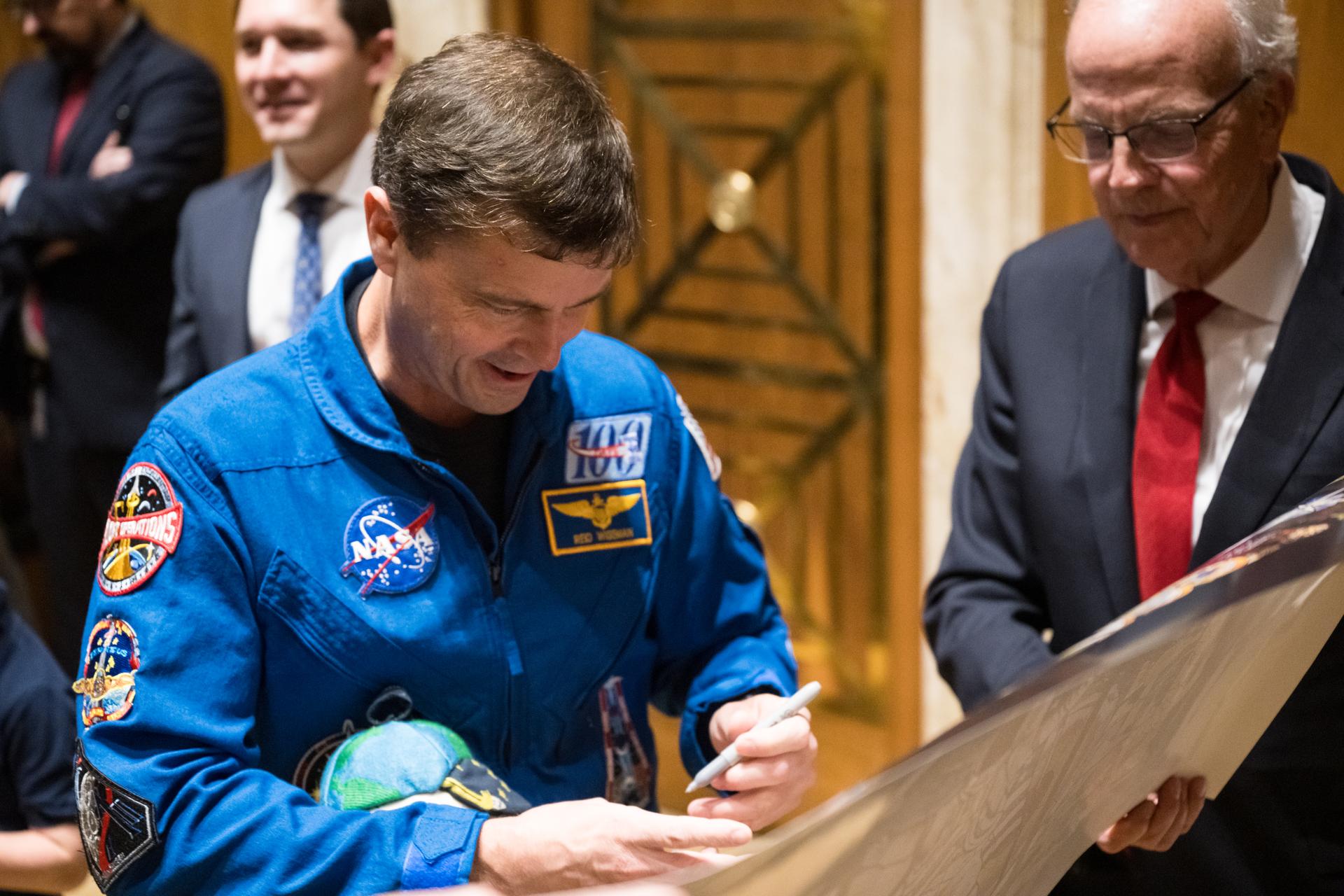 NASA astronaut Reid Wiseman, Artemis II commander signs a poster for U.S. Senator Jerry Moran (R-Kan.) at an event at the Dirksen Senate Office Building, Tuesday, May 12, 2026, in Washington. NASA’s Artemis II mission took Wiseman, and crewmates NASA astronaut Victor Glover, Artemis II pilot, Christina Koch, Artemis II mission specialist; and CSA (Canadian Space Agency) astronaut Jeremy Hansen, Artemis II mission specialist, on a nearly 10-day journey around the Moon and back to Earth in April 2026. Photo Credit: (NASA/Aubrey Gemignani)