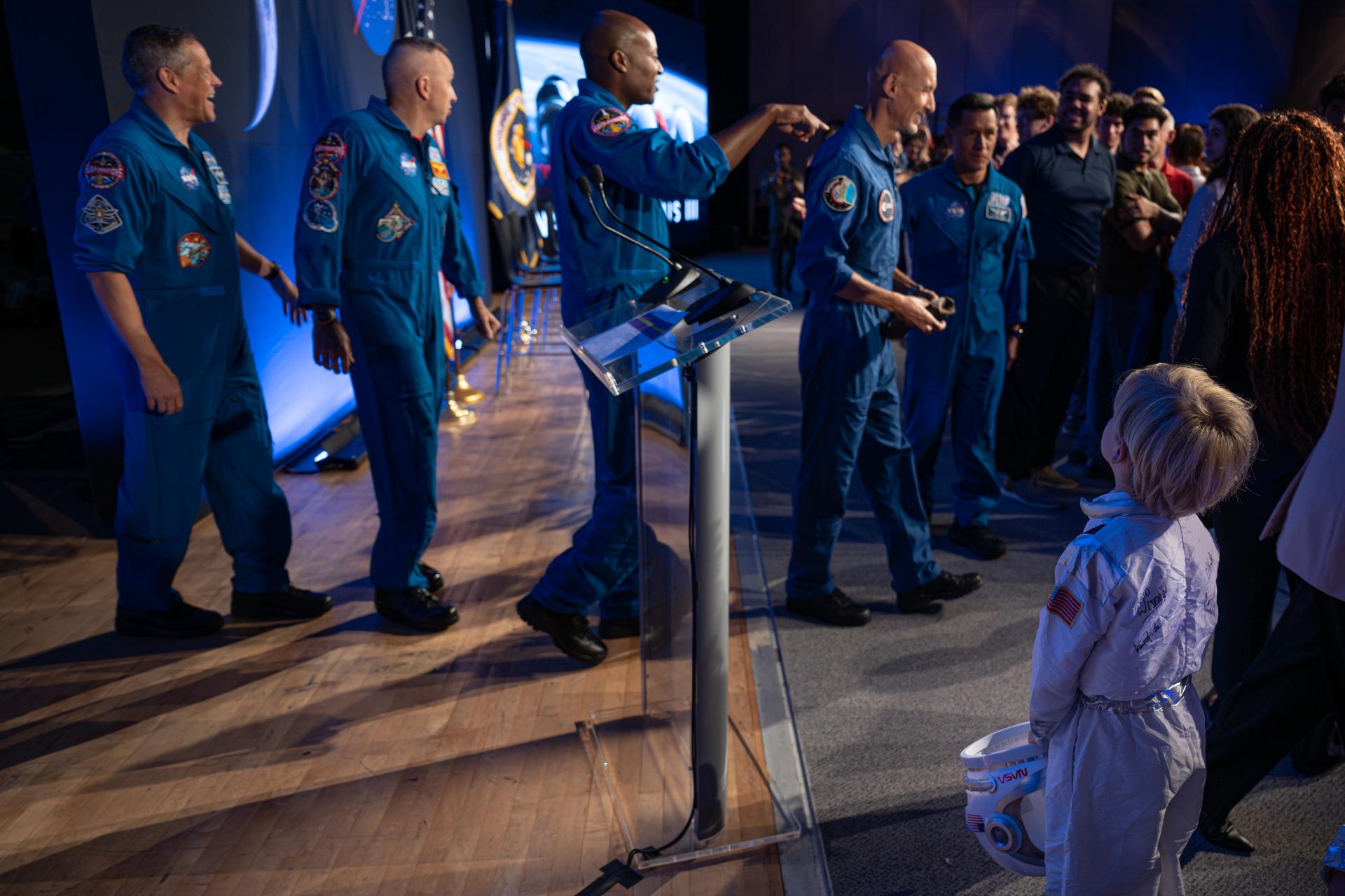A young space enthusiast dressed as an astronaut watches as Artemis III crew members NASA astronauts Bob Hines, backup crew member; Randy Bresnik, commander; Andre Douglas, mission specialist; ESA (European Space Agency) astronaut Luca Parmitano, pilot; and NASA astronaut Frank Rubio, mission specialist, appear on stage following the Artemis III crew announcement event, Tuesday, June 9, 2026, at NASA’s Johnson Space Center in Houston, Texas. Photo Credit: (NASA/John Kraus)