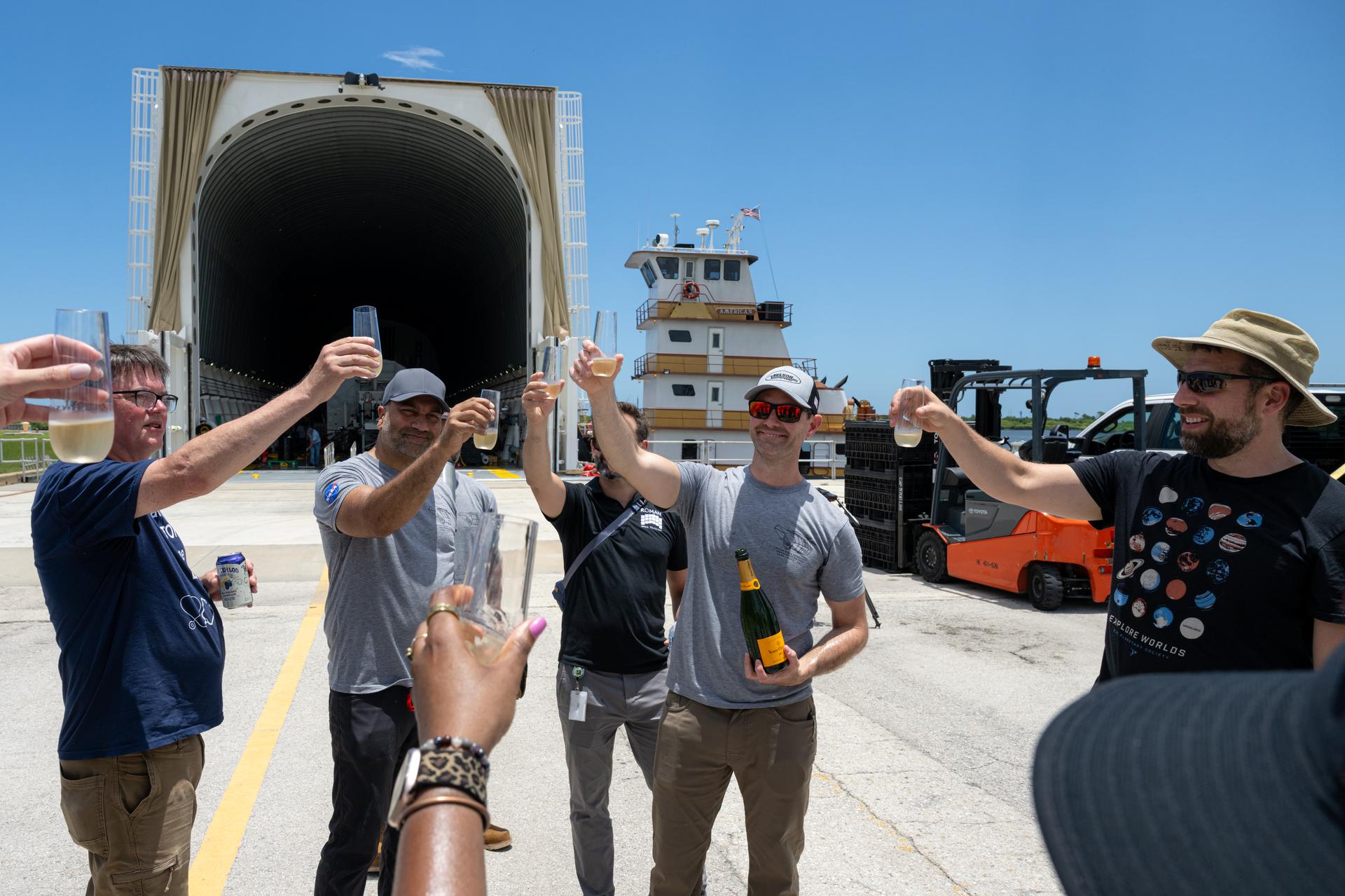 Members of the Nancy Grace Roman Space Telescope transport team celebrate with a toast following the arrival of NASA’s Pegasus barge, Sunday, June 21, at NASA’s Kennedy Space Center in Florida. The Pegasus barge delivered NASA’s Nancy Grace Roman Space Telescope and a weather cover for the Artemis III SLS (Space Launch System) rocket core stage to Kennedy. Photo Credit: (NASA/John Kraus)