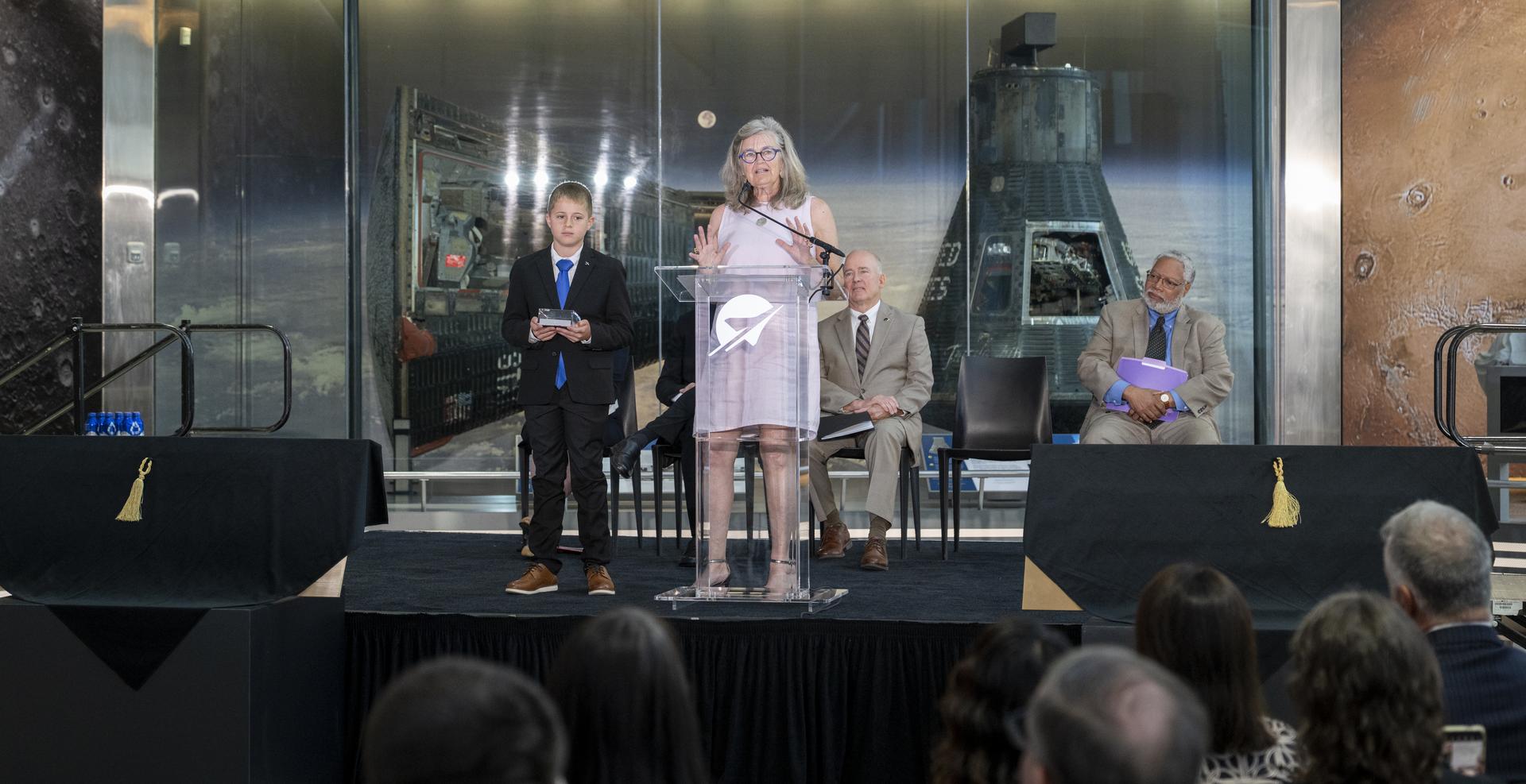 Wright brother’s great-grandniece Amanda Wright Lane, right, delivers remarks alongside her grandson Wren Wright Banhos, left, after accepting a swatch of muslin fabric from the original Wright Flyer the Wright Brothers used to make the first powered flight in 1903 on behalf of the Smithsonian’s National Air and Space Museum during the museum’s rededication ceremony Wednesday, July 1, 2026, in Washington. The swatch is being returned to the museum after having been flown aboard NASA’s Artemis II mission around the Moon and back to Earth in April 2026. Photo Credit: (NASA/Keegan Barber)