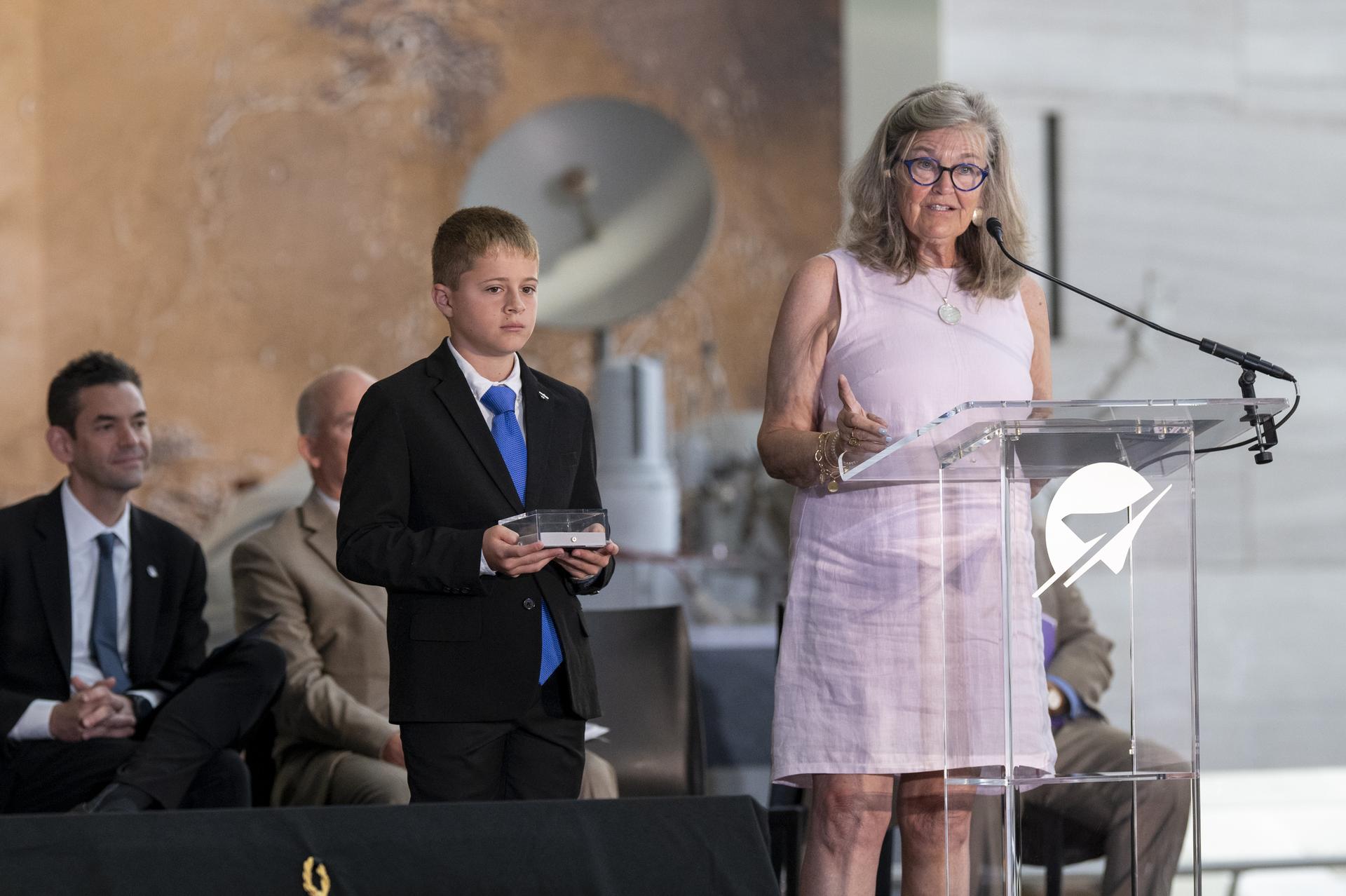 Wright brother’s great-grandniece Amanda Wright Lane, right, delivers remarks alongside her grandson Wren Wright Banhos, left, after accepting a swatch of muslin fabric from the original Wright Flyer the Wright Brothers used to make the first powered flight in 1903 on behalf of the Smithsonian’s National Air and Space Museum during the museum’s rededication ceremony Wednesday, July 1, 2026, in Washington. The swatch is being returned to the museum after having been flown aboard NASA’s Artemis II mission around the Moon and back to Earth in April 2026. Photo Credit: (NASA/Keegan Barber)