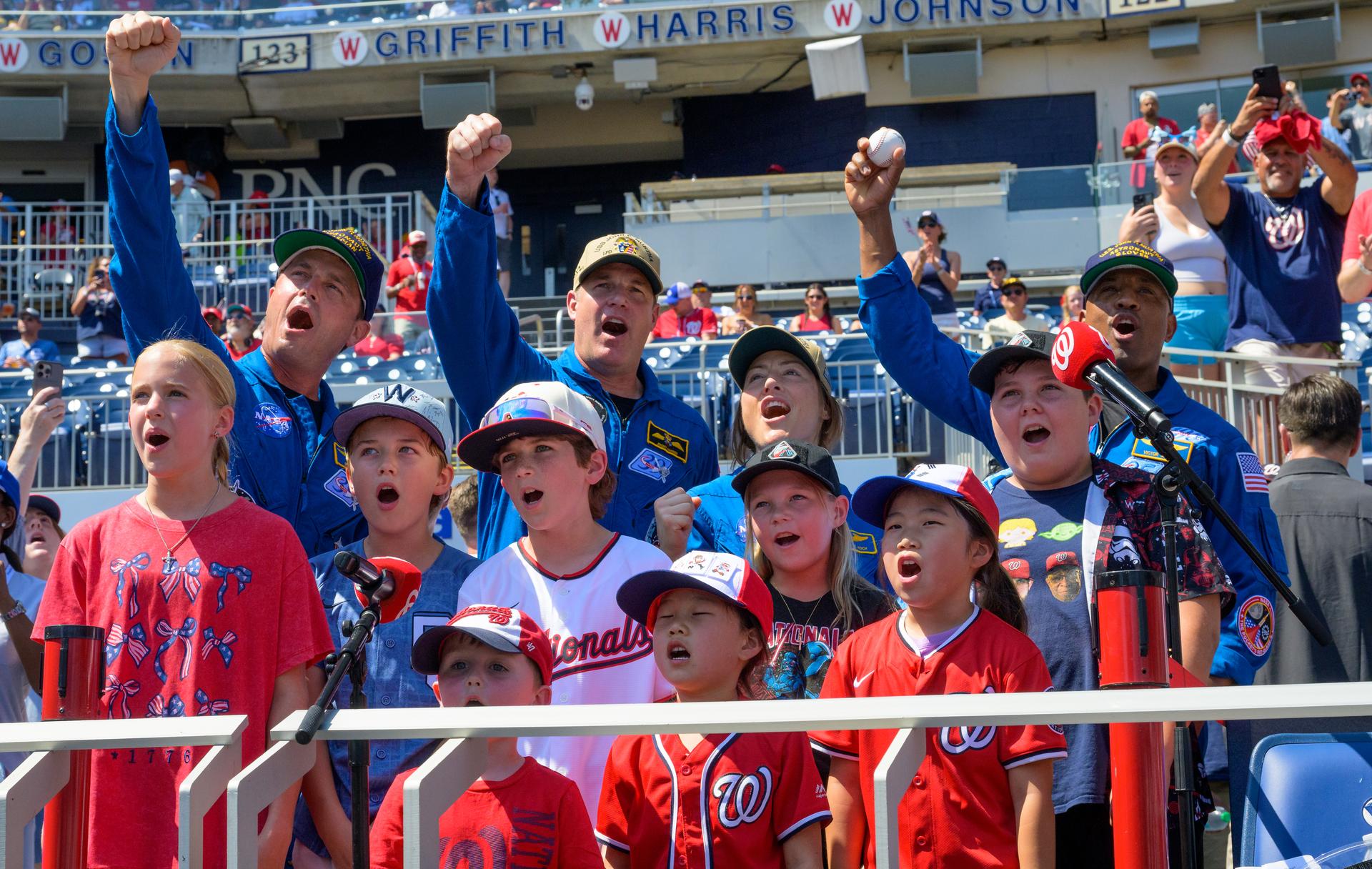 NASA astronaut Reid Wiseman, commander; left, CSA (Canadian Space Agency) astronaut Jeremy Hansen, mission specialist; Christina Koch, mission specialist; and Victor Glover, pilot, right, along with members of the Jr. Nats Kids Club, are seen as they give the call to “play ball” at the beginning of a baseball game between the Pittsburgh Pirates and the Washington Nationals, Saturday, July 4, 2026, at Nationals Park in Washington. NASA’s Artemis II mission took Wiseman, Glover, Koch, and Hansen on a nearly 10-day journey around the Moon and back to Earth in April 2026. Photo Credit: (NASA/Bill Ingalls)