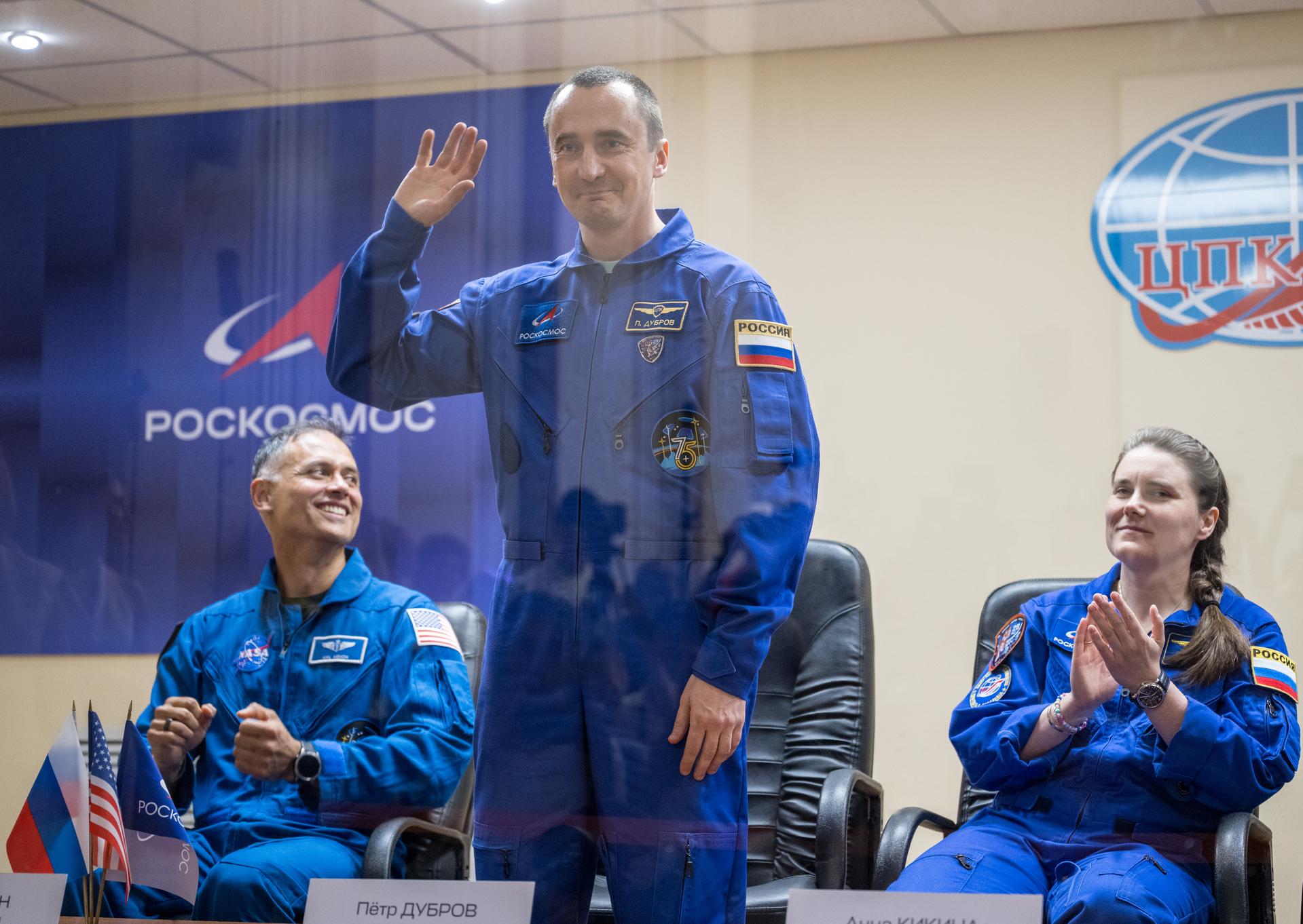 Expedition 75 crewmembers: NASA astronaut Anil Menon, left, Roscosmos cosmonauts Pyotr Dubrov and Anna Kikina, right, are seen in quarantine, behind glass, during a press conference, Monday, July 13, 2026 a the Cosmonaut Hotel in Baikonur, Kazakhstan. Menon, Dubrov, and Kikina are scheduled to launch aboard the Soyuz MS-29 spacecraft to the International Space Station on July 14. Photo Credit: (NASA/Bill Ingalls)