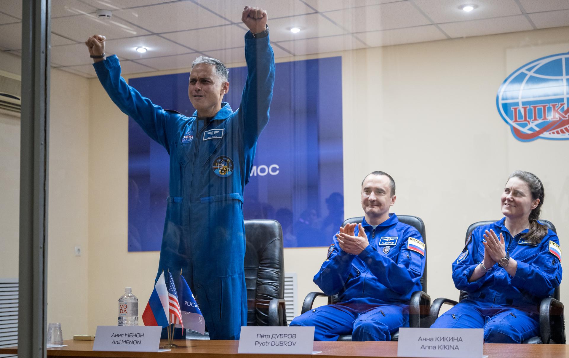 Expedition 75 crewmembers: NASA astronaut Anil Menon, left, Roscosmos cosmonauts Pyotr Dubrov and Anna Kikina, right, are seen in quarantine, behind glass, during a press conference, Monday, July 13, 2026 a the Cosmonaut Hotel in Baikonur, Kazakhstan. Menon, Dubrov, and Kikina are scheduled to launch aboard the Soyuz MS-29 spacecraft to the International Space Station on July 14. Photo Credit: (NASA/Bill Ingalls)