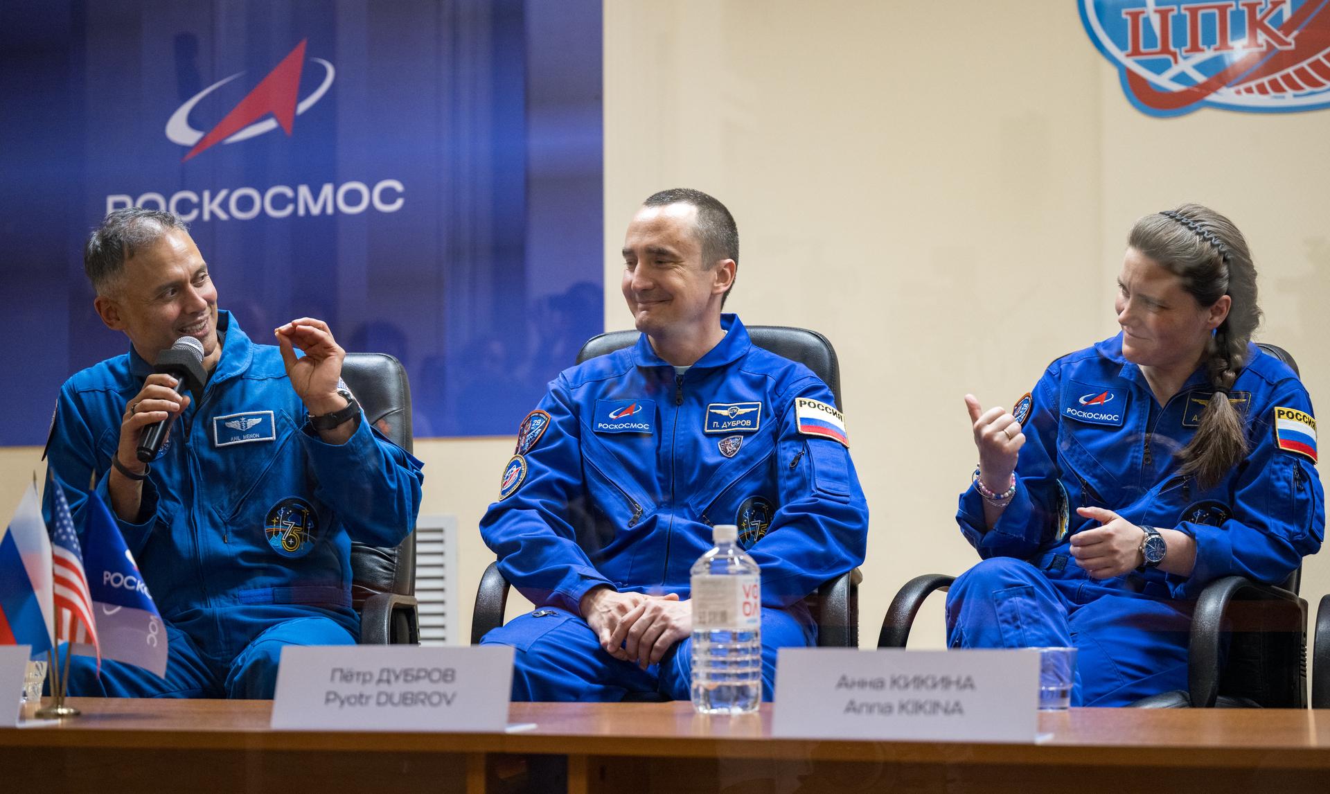 Expedition 75 crewmembers: NASA astronaut Anil Menon, left, Roscosmos cosmonauts Pyotr Dubrov and Anna Kikina, right, are seen in quarantine, behind glass, during a press conference, Monday, July 13, 2026 a the Cosmonaut Hotel in Baikonur, Kazakhstan. Menon, Dubrov, and Kikina are scheduled to launch aboard the Soyuz MS-29 spacecraft to the International Space Station on July 14. Photo Credit: (NASA/Bill Ingalls)