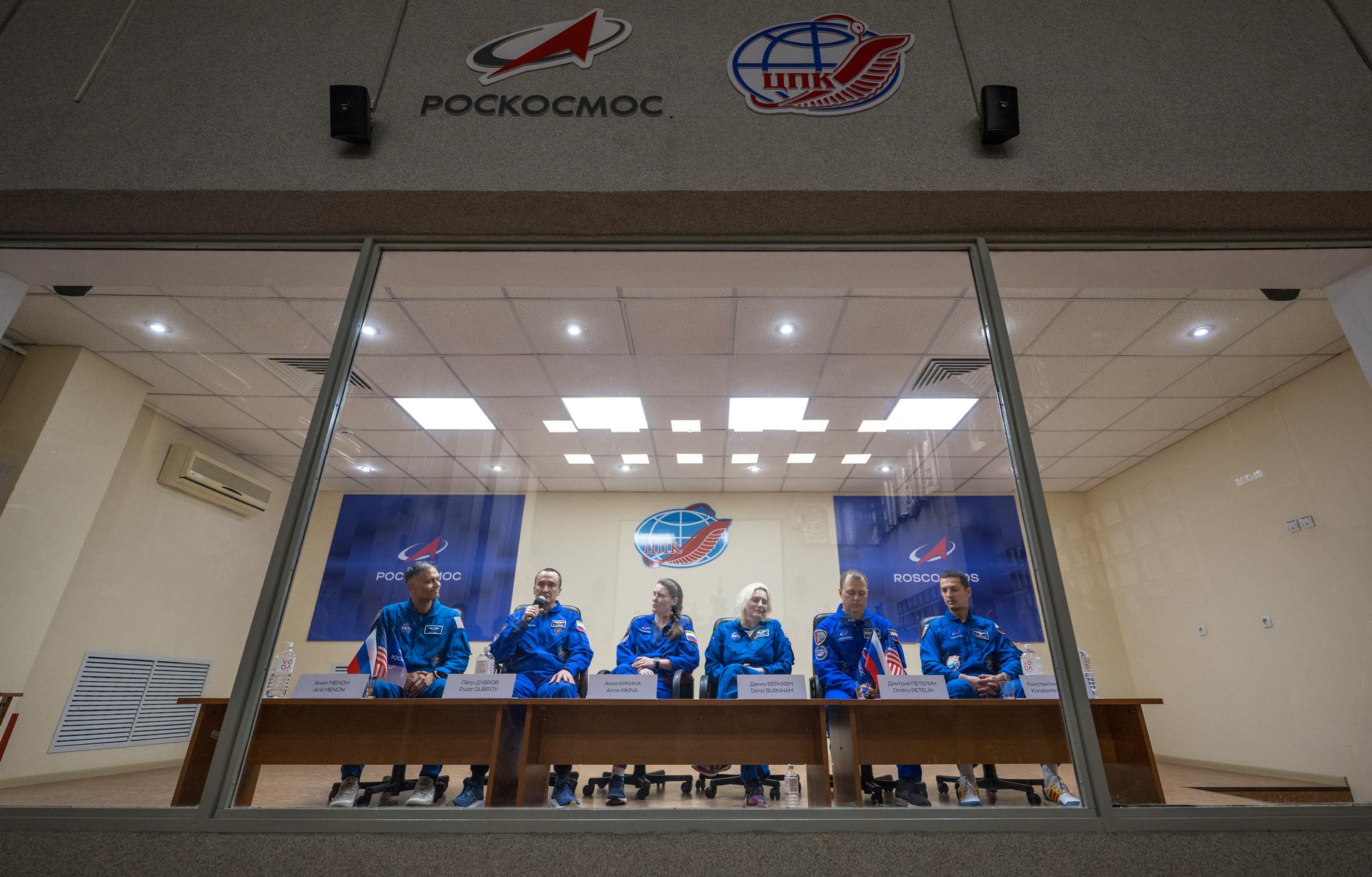 Expedition 75 crewmembers: NASA astronaut Anil Menon, left, Roscosmos cosmonauts Pyotr Dubrov and Anna Kikina, along with backup crewmemebers: NASA astronaut Deniz Burnham, Roscosmos cosmonauts Dmitry Petelin, and Konstantin Borisov, right, are seen in quarantine, behind glass, during a press conference, Monday, July 13, 2026 a the Cosmonaut Hotel in Baikonur, Kazakhstan. Menon, Dubrov, and Kikina are scheduled to launch aboard the Soyuz MS-29 spacecraft to the International Space Station on July 14. Photo Credit: (NASA/Bill Ingalls)