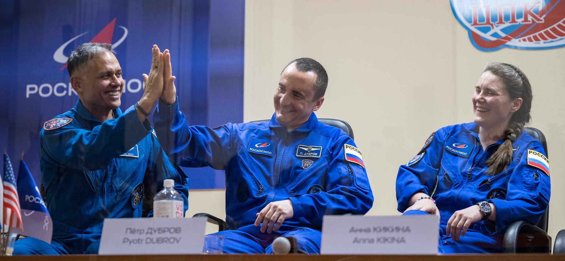 Expedition 75 crewmembers: NASA astronaut Anil Menon, left, Roscosmos cosmonauts Pyotr Dubrov and Anna Kikina, right, are seen in quarantine, behind glass, during a press conference, Monday, July 13, 2026 a the Cosmonaut Hotel in Baikonur, Kazakhstan. Menon, Dubrov, and Kikina are scheduled to launch aboard the Soyuz MS-29 spacecraft to the International Space Station on July 14. Photo Credit: (NASA/Bill Ingalls)