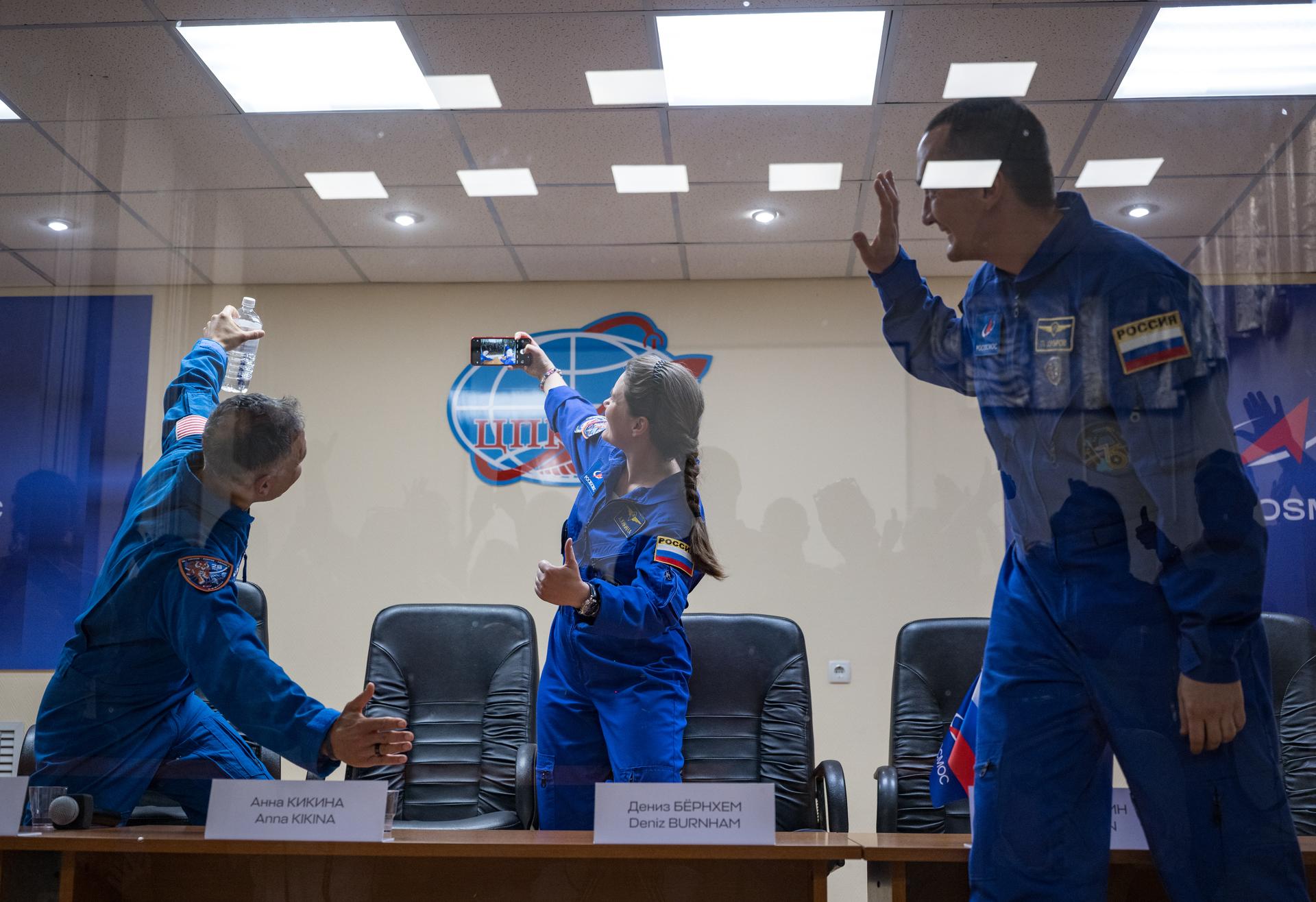 Expedition 75 crewmembers: NASA astronaut Anil Menon, left, Roscosmos cosmonauts Anna Kikina, and Pyotr Dubrov, right, are seen in quarantine, behind glass, during a press conference, Monday, July 13, 2026 a the Cosmonaut Hotel in Baikonur, Kazakhstan. Menon, Dubrov, and Kikina are scheduled to launch aboard the Soyuz MS-29 spacecraft to the International Space Station on July 14. Photo Credit: (NASA/Bill Ingalls)
