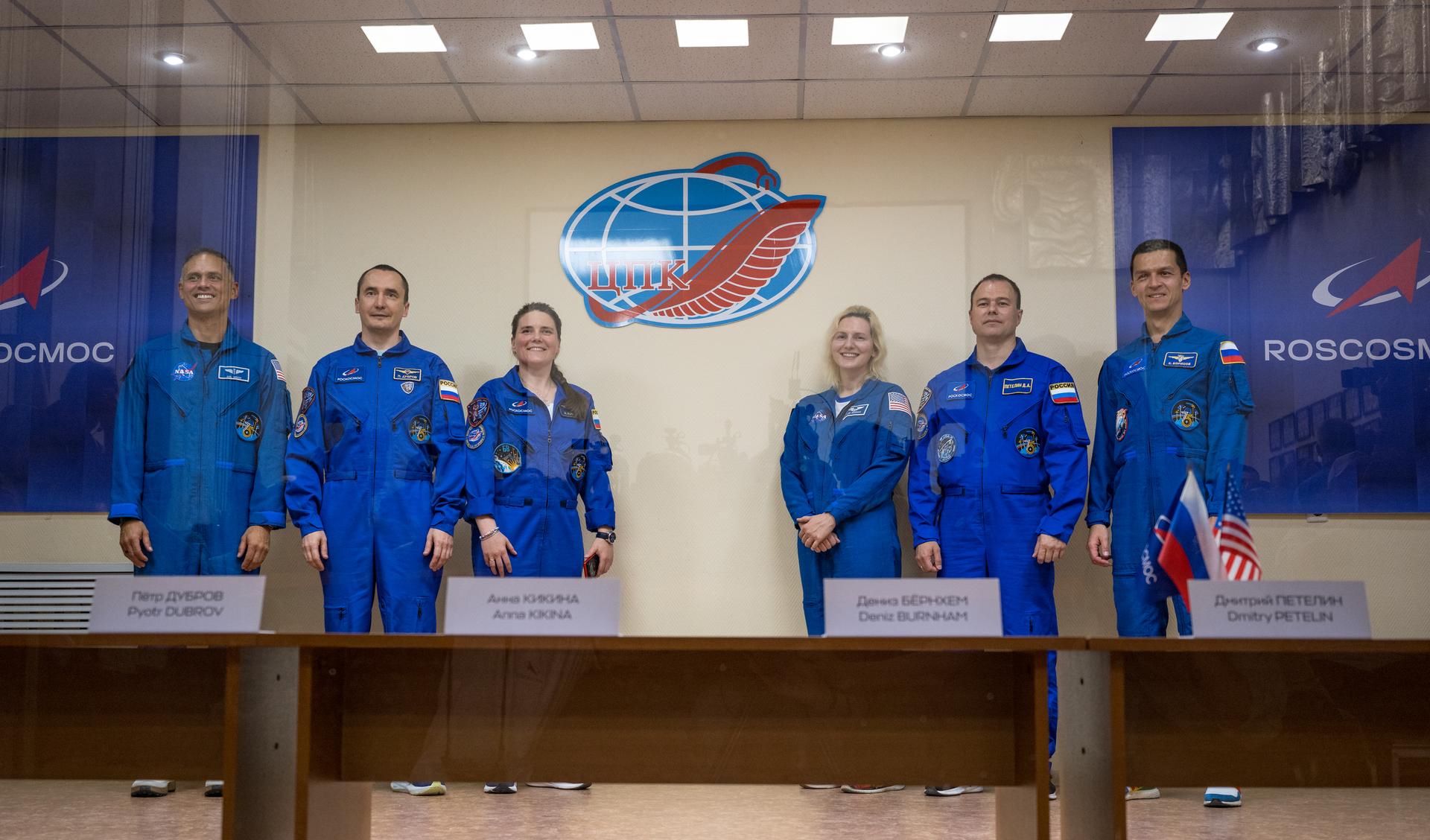 Expedition 75 crewmembers: NASA astronaut Anil Menon, left, Roscosmos cosmonauts Pyotr Dubrov and Anna Kikina, along with backup crewmemebers: NASA astronaut Deniz Burnham, Roscosmos cosmonauts Dmitry Petelin, and Konstantin Borisov, right, are seen in quarantine, behind glass, during a press conference, Monday, July 13, 2026 a the Cosmonaut Hotel in Baikonur, Kazakhstan. Menon, Dubrov, and Kikina are scheduled to launch aboard the Soyuz MS-29 spacecraft to the International Space Station on July 14. Photo Credit: (NASA/Bill Ingalls)