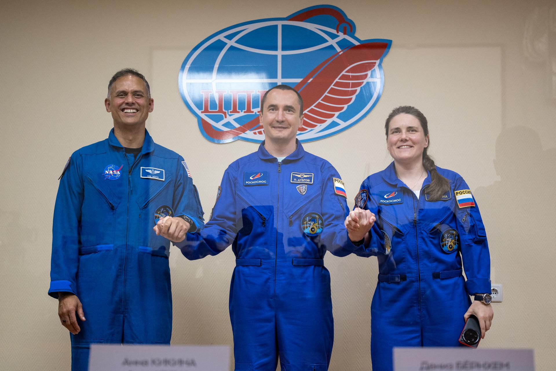 Expedition 75 crewmembers: NASA astronaut Anil Menon, left, Roscosmos cosmonauts Pyotr Dubrov, and Anna Kikina, right, are seen in quarantine, behind glass, during a press conference, Monday, July 13, 2026 a the Cosmonaut Hotel in Baikonur, Kazakhstan. Menon, Dubrov, and Kikina are scheduled to launch aboard the Soyuz MS-29 spacecraft to the International Space Station on July 14. Photo Credit: (NASA/Bill Ingalls)