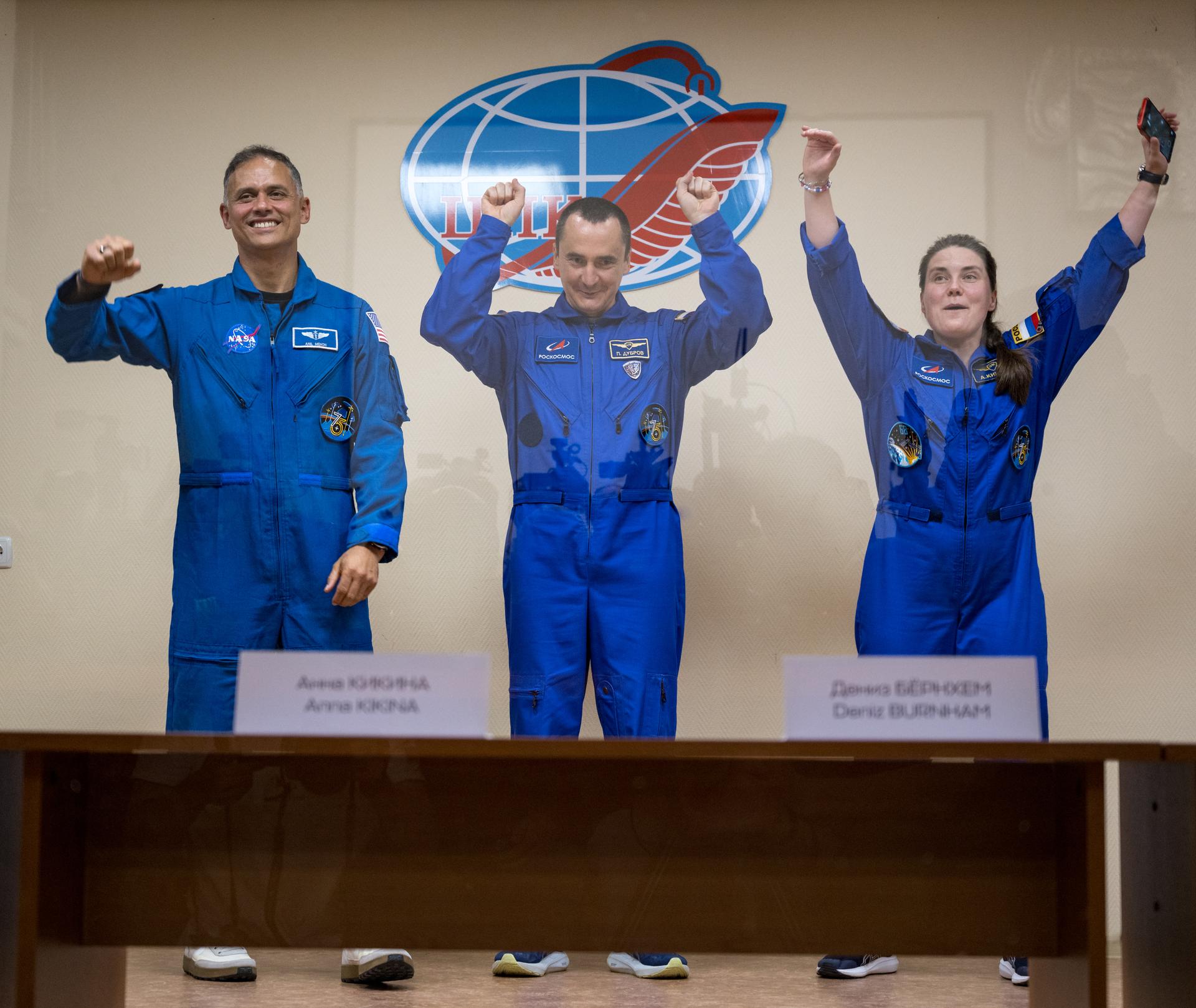 Expedition 75 crewmembers: NASA astronaut Anil Menon, left, Roscosmos cosmonauts Pyotr Dubrov, and Anna Kikina, right, are seen in quarantine, behind glass, during a press conference, Monday, July 13, 2026 a the Cosmonaut Hotel in Baikonur, Kazakhstan. Menon, Dubrov, and Kikina are scheduled to launch aboard the Soyuz MS-29 spacecraft to the International Space Station on July 14. Photo Credit: (NASA/Bill Ingalls)