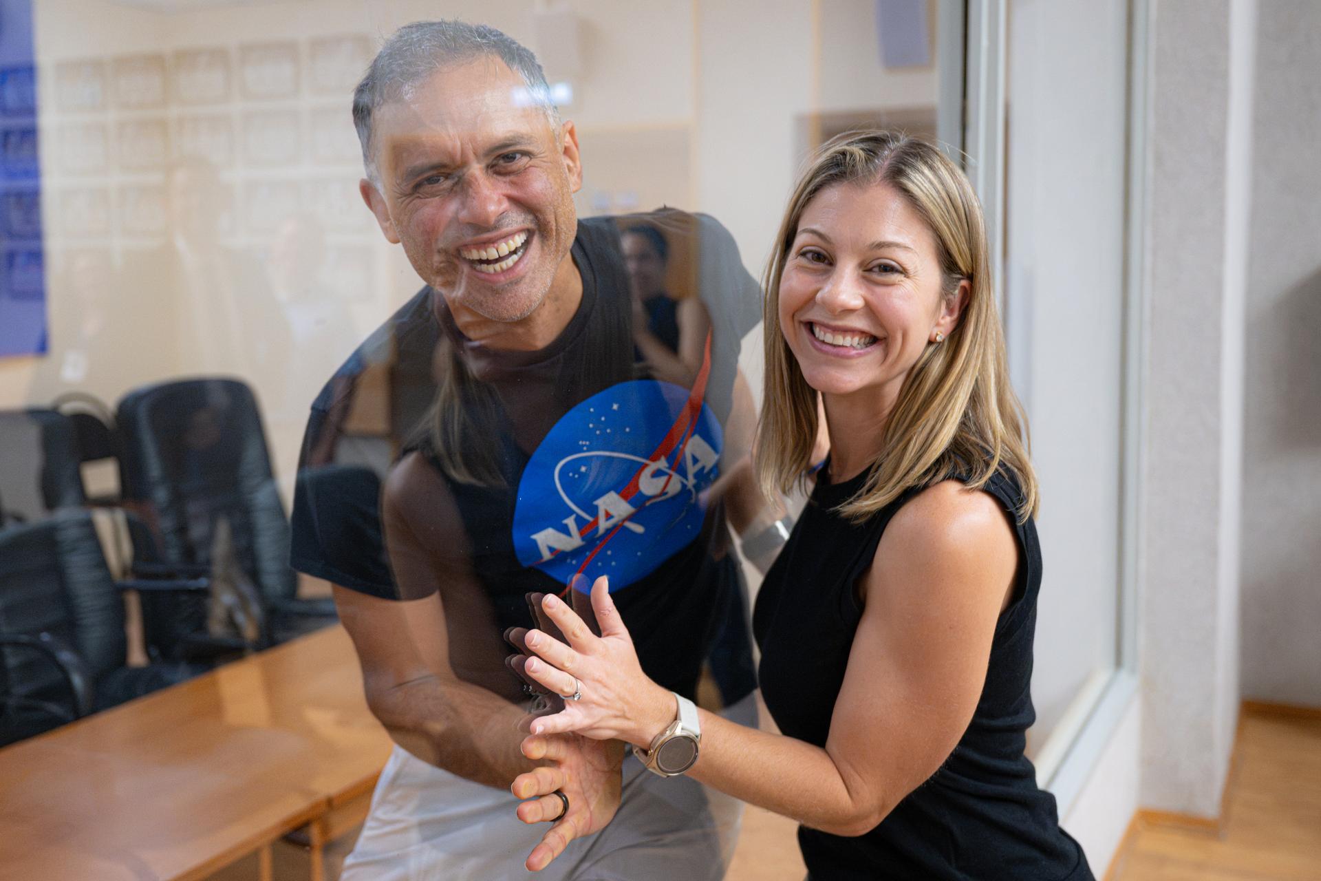 NASA astronaut and Expedition 75 crewmember Anil Menon, left, and his wife, NASA astronaut candidate Anna Menon, right, pose for a photograph between glass, Monday, July 13, 2026, at the Cosmonaut Hotel in Baikonur, Kazakhstan. Expedition 75 crewmembers NASA astronaut Anil Menon and Roscosmos cosmonauts Pyotr Dubrov and Anna Kikina are scheduled to launch aboard the Soyuz MS-29 spacecraft to the International Space Station on July 14. Photo Credit: (NASA/John Kraus)