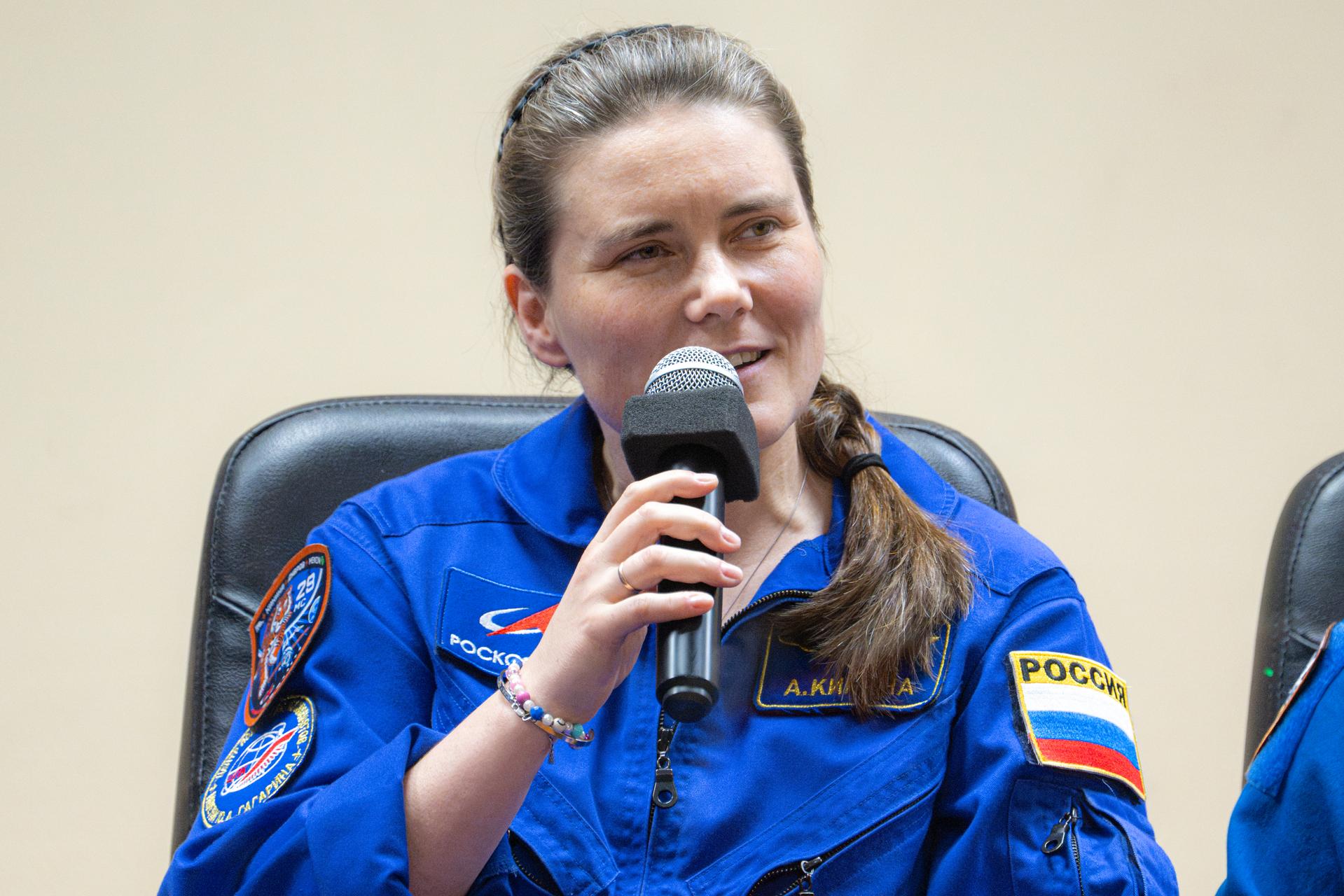 Expedition 75 crewmember Anna Kikina of Roscosmos is seen in quarantine, behind glass, during a press conference, Monday, July 13, 2026, at the Cosmonaut Hotel in Baikonur, Kazakhstan. Expedition 75 crewmembers NASA astronaut Anil Menon and Roscosmos cosmonauts Pyotr Dubrov and Anna Kikina are scheduled to launch aboard the Soyuz MS-29 spacecraft to the International Space Station on July 14. Photo Credit: (NASA/John Kraus)