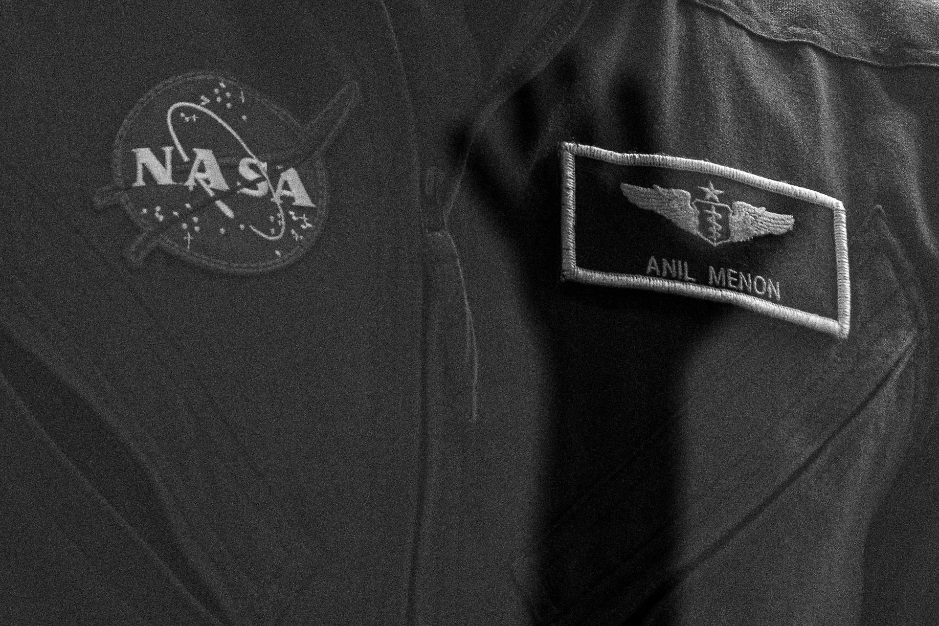 The shadow of an audience member's hand is cast onto the flight suit of NASA astronaut Anil Menon in quarantine, behind glass, during a press conference, Monday, July 13, 2026, at the Cosmonaut Hotel in Baikonur, Kazakhstan. Expedition 75 crewmembers NASA astronaut Anil Menon and Roscosmos cosmonauts Pyotr Dubrov and Anna Kikina are scheduled to launch aboard the Soyuz MS-29 spacecraft to the International Space Station on July 14. Photo Credit: (NASA/John Kraus)