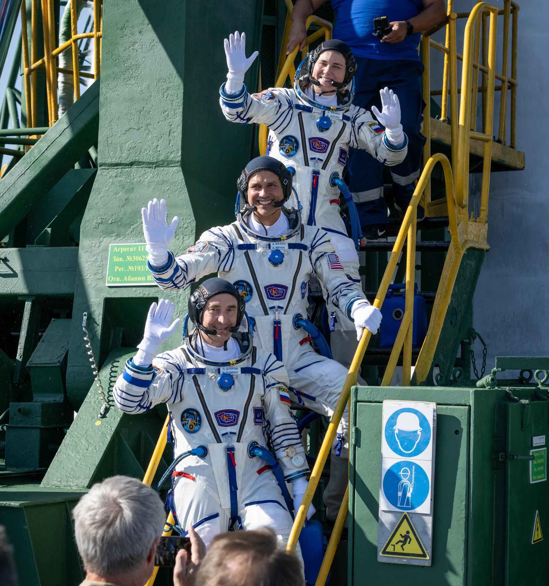 Expedition 75 Roscosmos cosmonaut Anna Kikina, top, NASA astronaut Anil Menon, middle, and Roscosmos cosmonaut Pyotr Dubrov, bottom, wave farewell prior to boarding the Soyuz MS-29 spacecraft for launch, Tuesday, July 14, 2026 at the Baikonur Cosmodrome in Kazakhstan. Launch of the Soyuz rocket will send the trio on a mission to the International Space Station. Photo Credit: (NASA/Bill Ingalls)
