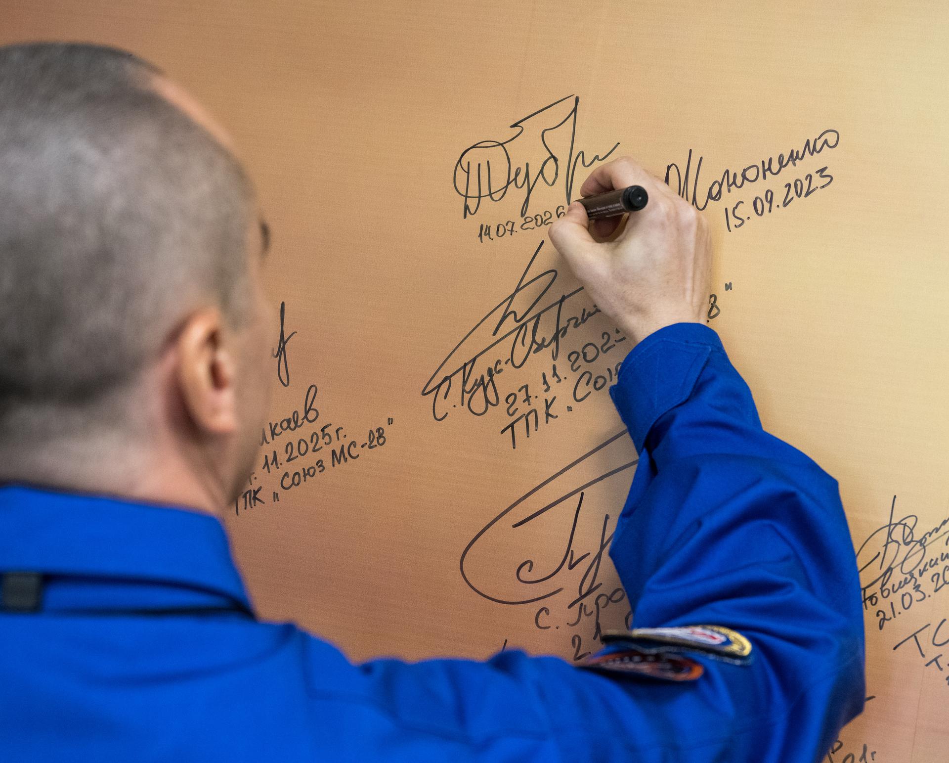 Roscosmos cosmonaut Pyotr Dubrov signs a mural at the Cosmonaut Hotel prior to departing for suit-up and launch on a Soyuz rocket with fellow crewmates Roscosmos cosmonaut Anna Kikina, and NASA astronaut Anil Menon, Tuesday, July 14, 2026, in Baikonur, Kazakhstan. The launch will send Menon, Dubrov, and Kikina on a mission to the International Space Station. Photo Credit: (NASA/Bill Ingalls)