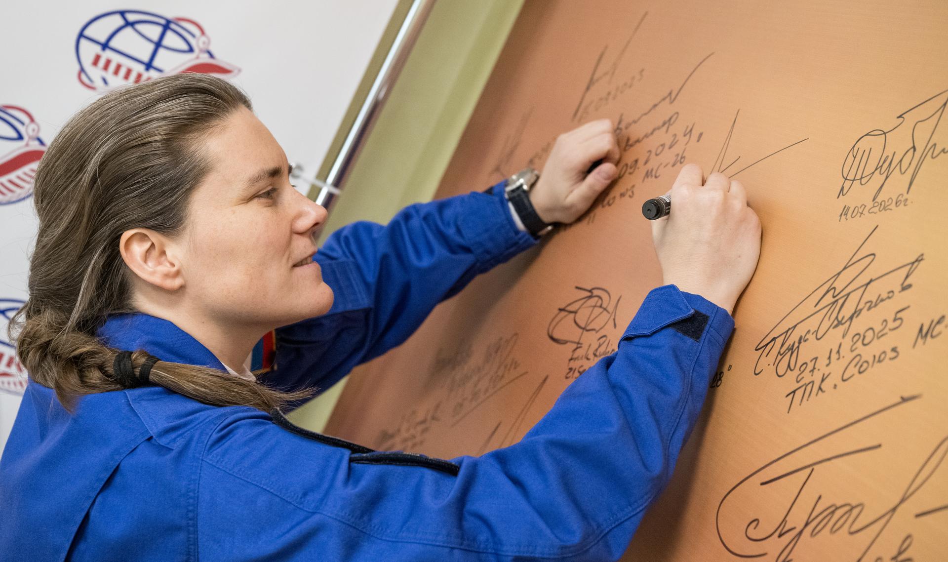 Roscosmos cosmonaut Anna Kikina signs a mural at the Cosmonaut Hotel prior to departing for suit-up and launch on a Soyuz rocket with fellow crewmates Roscosmos cosmonaut Pyotr Dubrov, and NASA astronaut Anil Menon, Tuesday, July 14, 2026, in Baikonur, Kazakhstan. The launch will send Menon, Dubrov, and Kikina on a mission to the International Space Station. Photo Credit: (NASA/Bill Ingalls)