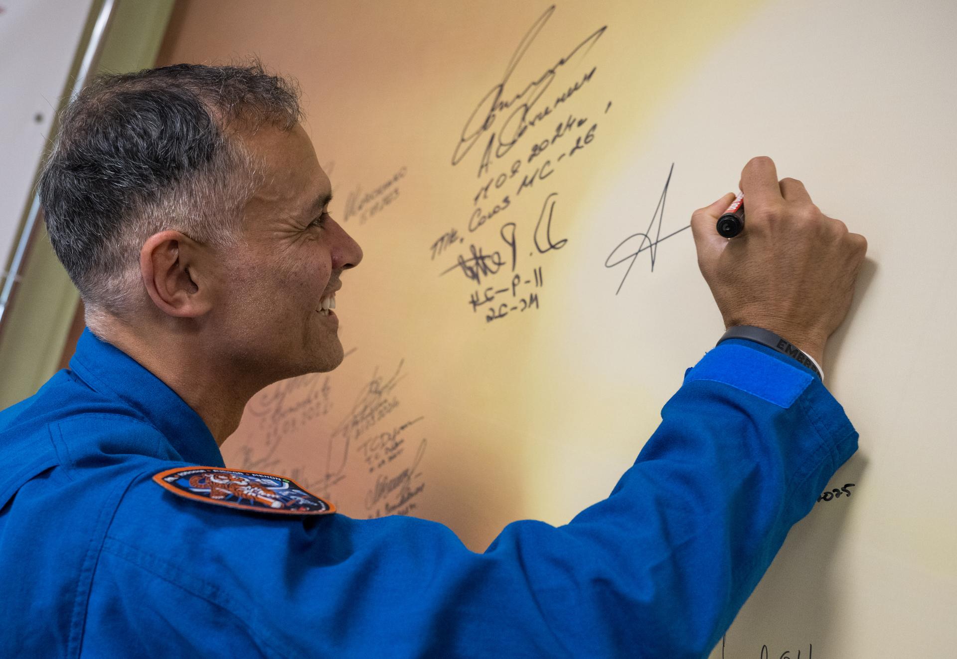 NASA astronaut Anil Menon signs a mural at the Cosmonaut Hotel prior to departing for suit-up and launch on a Soyuz rocket with fellow crewmates Roscosmos cosmonauts Anna Kikina, and Pyotr Dubrov, Tuesday, July 14, 2026, in Baikonur, Kazakhstan. The launch will send Menon, Dubrov, and Kikina on a mission to the International Space Station. Photo Credit: (NASA/Bill Ingalls)