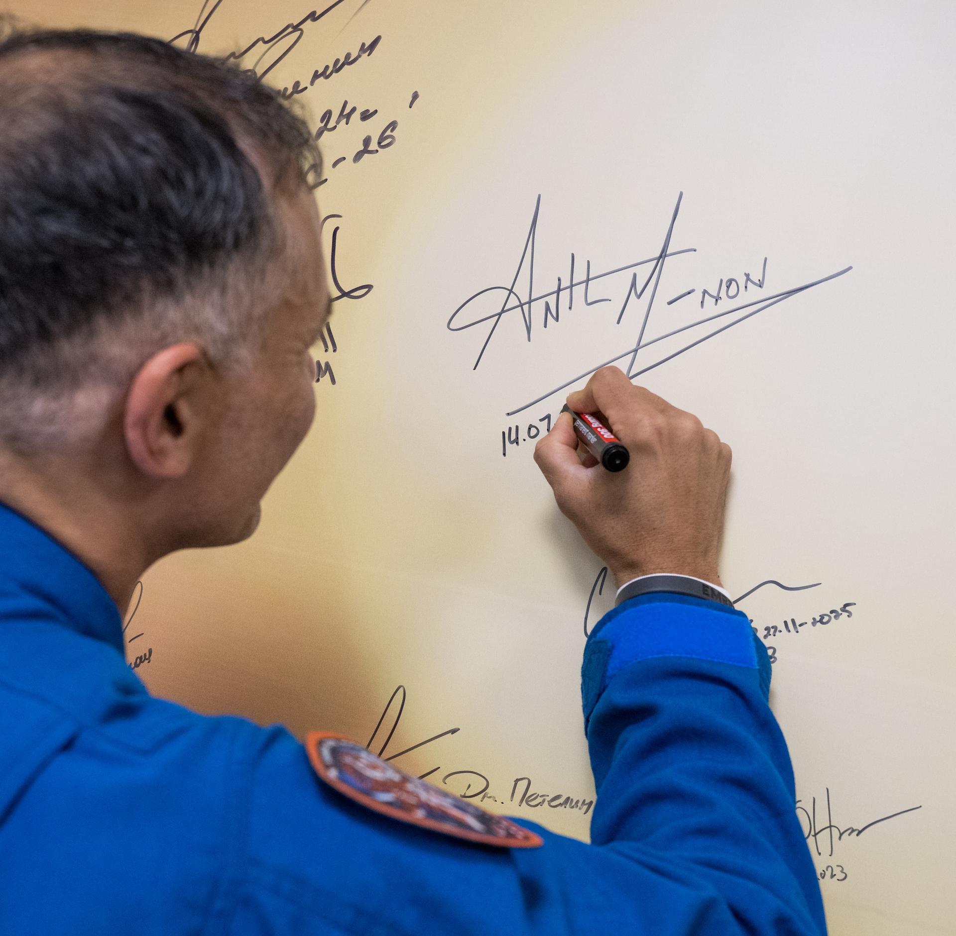 NASA astronaut Anil Menon signs a mural at the Cosmonaut Hotel prior to departing for suit-up and launch on a Soyuz rocket with fellow crewmates Roscosmos cosmonauts Anna Kikina, and Pyotr Dubrov, Tuesday, July 14, 2026, in Baikonur, Kazakhstan. The launch will send Menon, Dubrov, and Kikina on a mission to the International Space Station. Photo Credit: (NASA/Bill Ingalls)