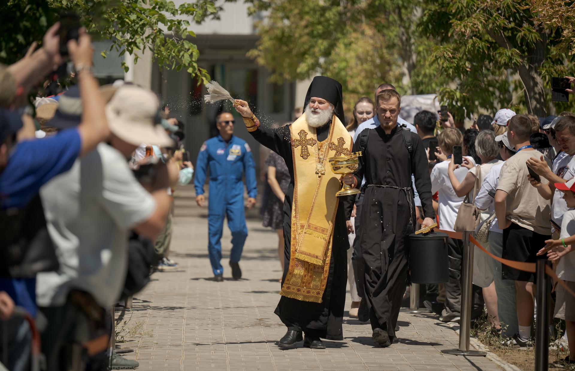 A Russian Orthodox Priest blesses onlookers as the Expedition 75 crew prepares to depart the Cosmonaut Hotel to suit-up for their Soyuz launch, Tuesday, July 14, 2026, in Baikonur, Kazakhstan. The launch will send Expedition 75 crewmembers: NASA astronaut Anil Menon, and Roscosmos cosmonauts Pyotr Dubrov, and Anna Kikina, on a mission to the International Space Station. Photo Credit: (NASA/Bill Ingalls)
