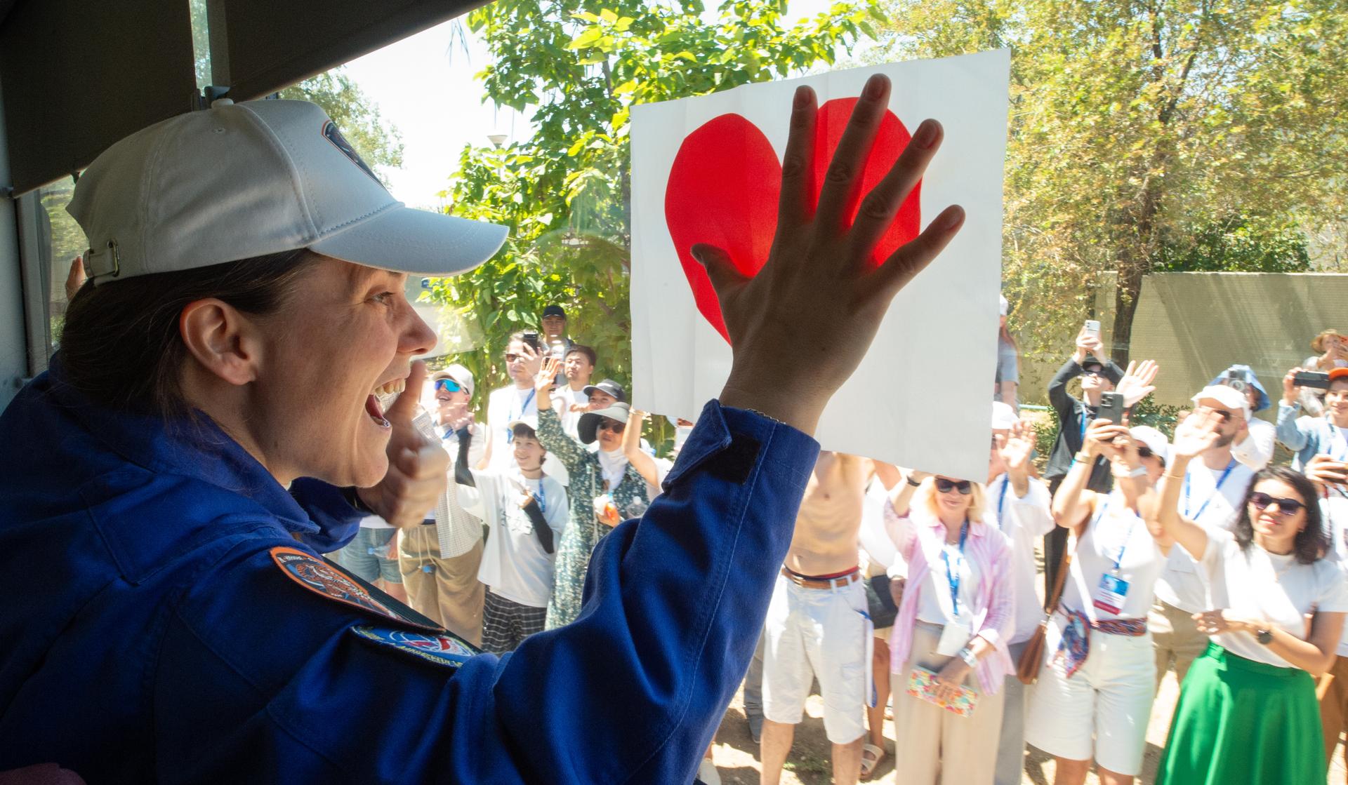 Expedition 75 Roscosmos cosmonaut Anna Kikina waves as she departs the Cosmonaut Hotel with crew mates Roscosmos cosmonaut Pyotr Dubrov, and NASA astronaut Anil Menon, to suit-up for their Soyuz launch, Tuesday, July 14, 2026, in Baikonur, Kazakhstan. The launch will send Menon, Dubrov, and Kikina on a mission to the International Space Station. Photo Credit: (NASA/GCTC/Pavel Shvets)