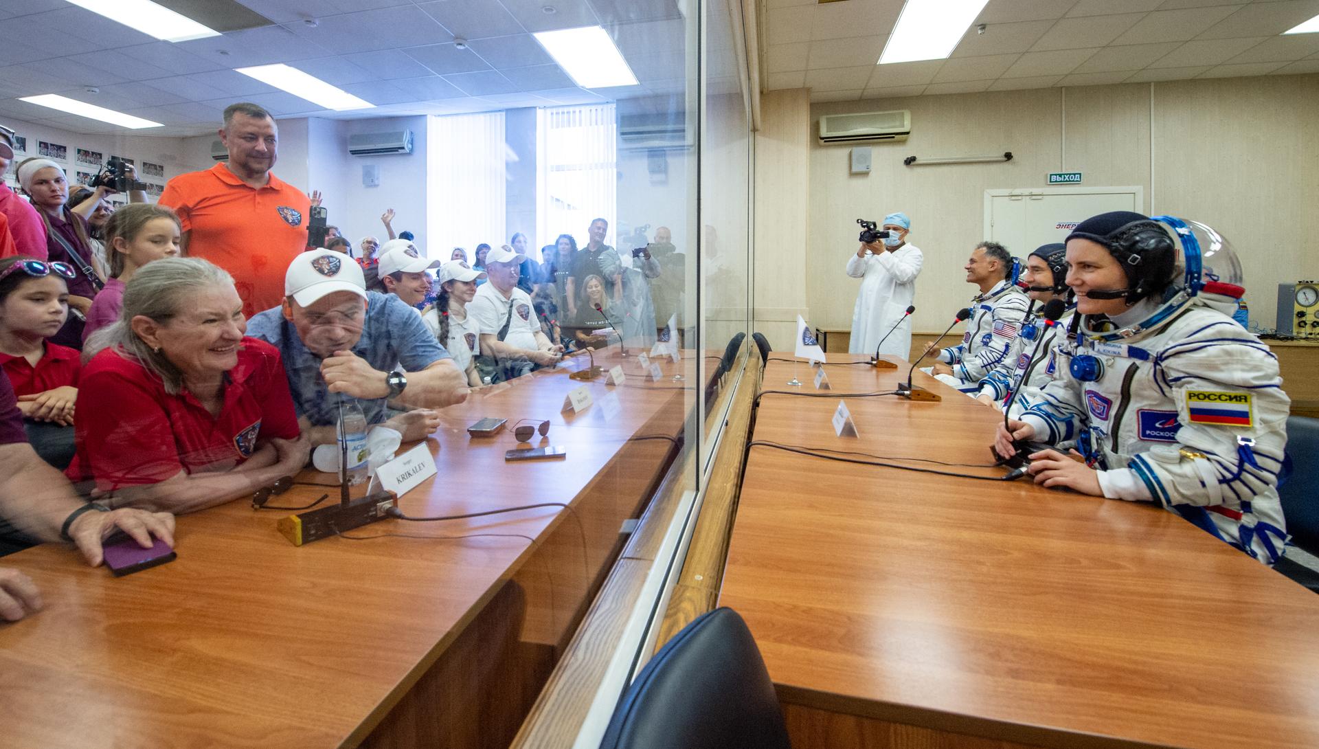 Expedition 75 Roscosmos cosmonaut Anna Kikina, foreground, Roscosmos cosmonaut Pyotr Dubrov, and NASA astronaut Anil Menon, left, talk with friends and family after having their Russian Sokol suits pressure checked as they prepare for their Soyuz launch to the International Space Station Tuesday, July 14, 2026 in Baikonur, Kazakhstan. Photo Credit: (NASA/GCTC/Pavel Shvets)