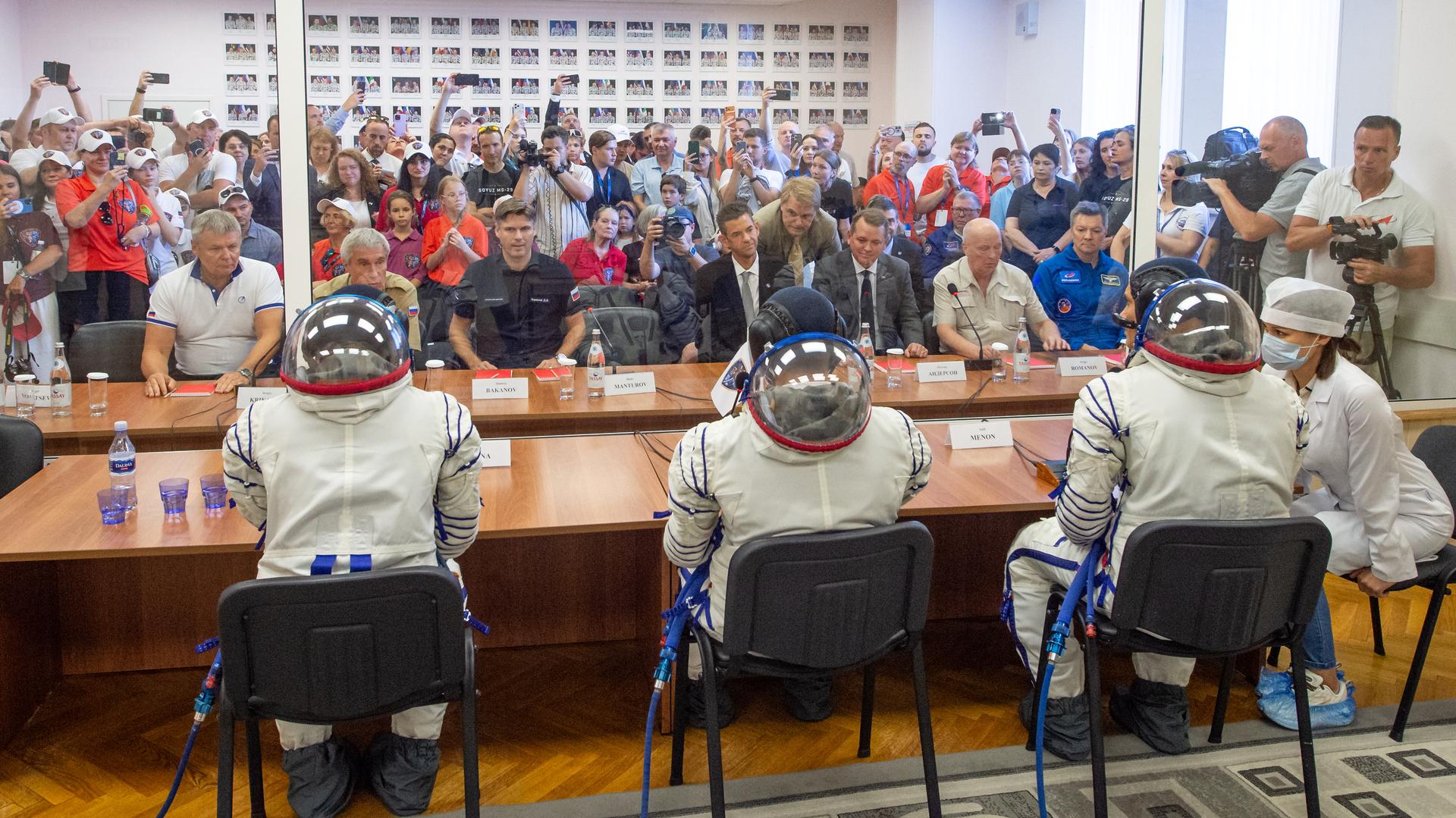Expedition 75 Roscosmos cosmonaut Anna Kikina, left, Roscosmos cosmonaut Pyotr Dubrov, and NASA astronaut Anil Menon, right, talk with Roscosmos Director of Human Spaceflight Programs Sergei Krikalev, seated 2nd from left, Roscosmos Director General Dmitry Bakanov, seated 3rd from left, NASA Administrator Jared Isaacman, and NASA Deputy Administrator Matt Anderson, 5th from left, after having their Russian Sokol suits pressure checked as they prepare for their Soyuz launch to the International Space Station Tuesday, July 14, 2026 in Baikonur, Kazakhstan. Photo Credit: (NASA/GCTC/Pavel Shvets)